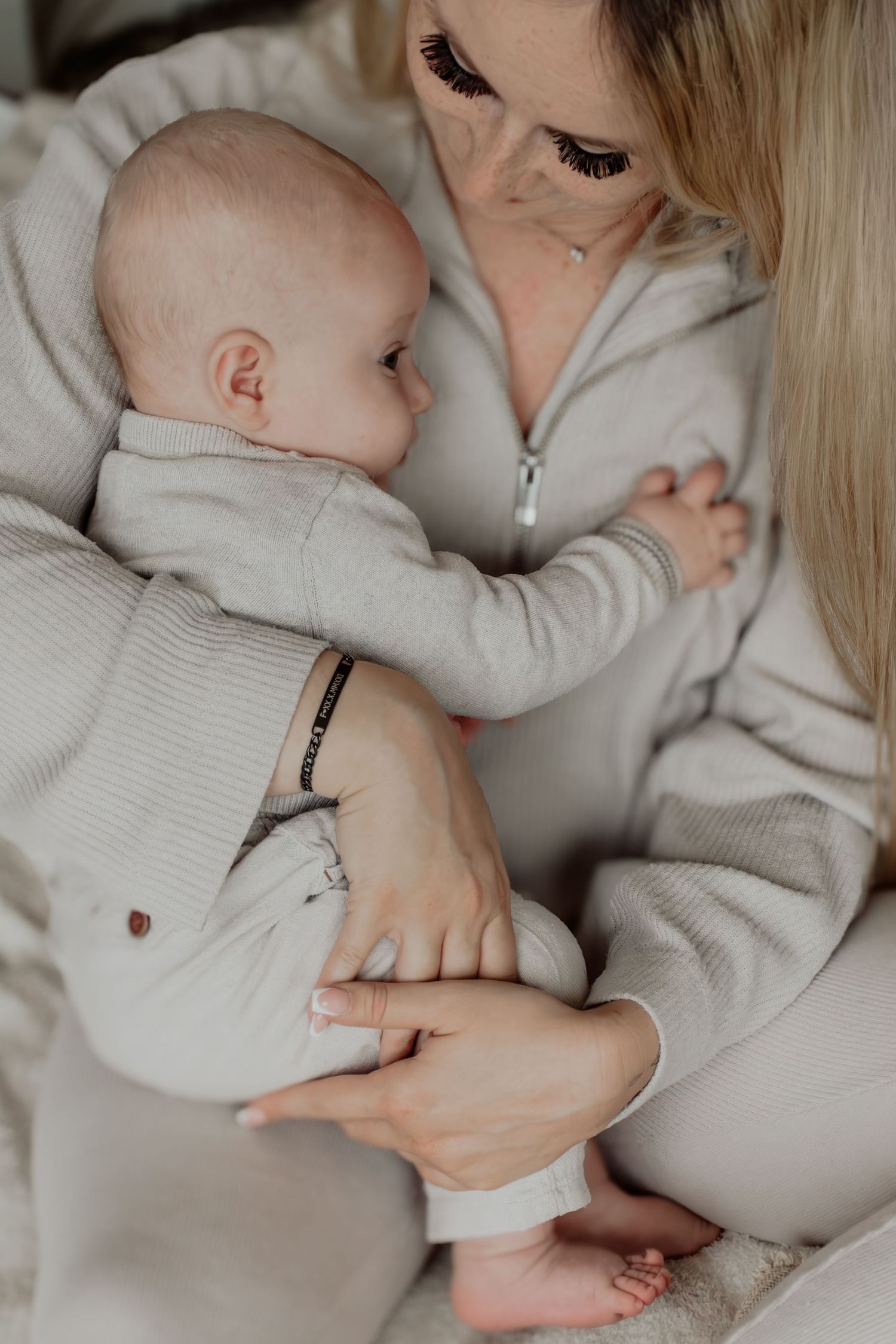 A baby in a white knit sweater rests against someone wearing a beige sweater in a series of tender moments.