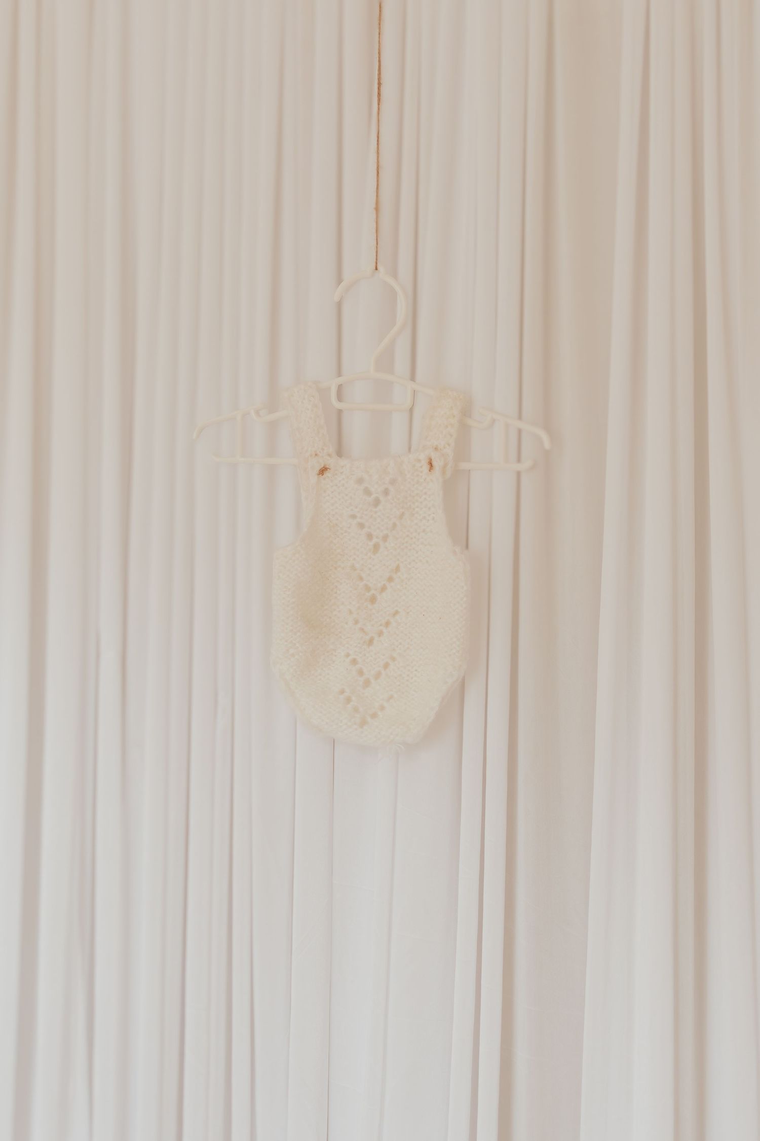 Neugeborener weißer Strickkörper, der an Schnüren an einer hellen Wand hängt, schafft ein elegantes dekoratives Display.