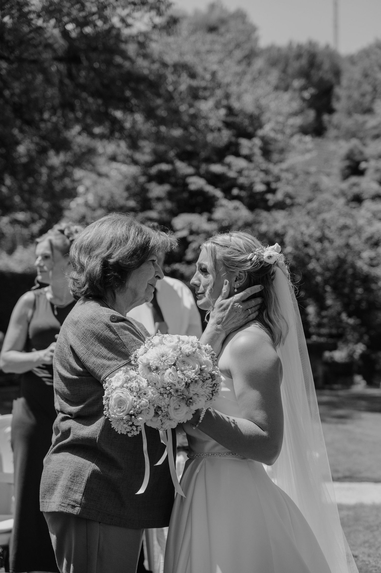 Emotional black and white photo of a bride receiving a tender kiss on the cheek from an older woman at her wedding.