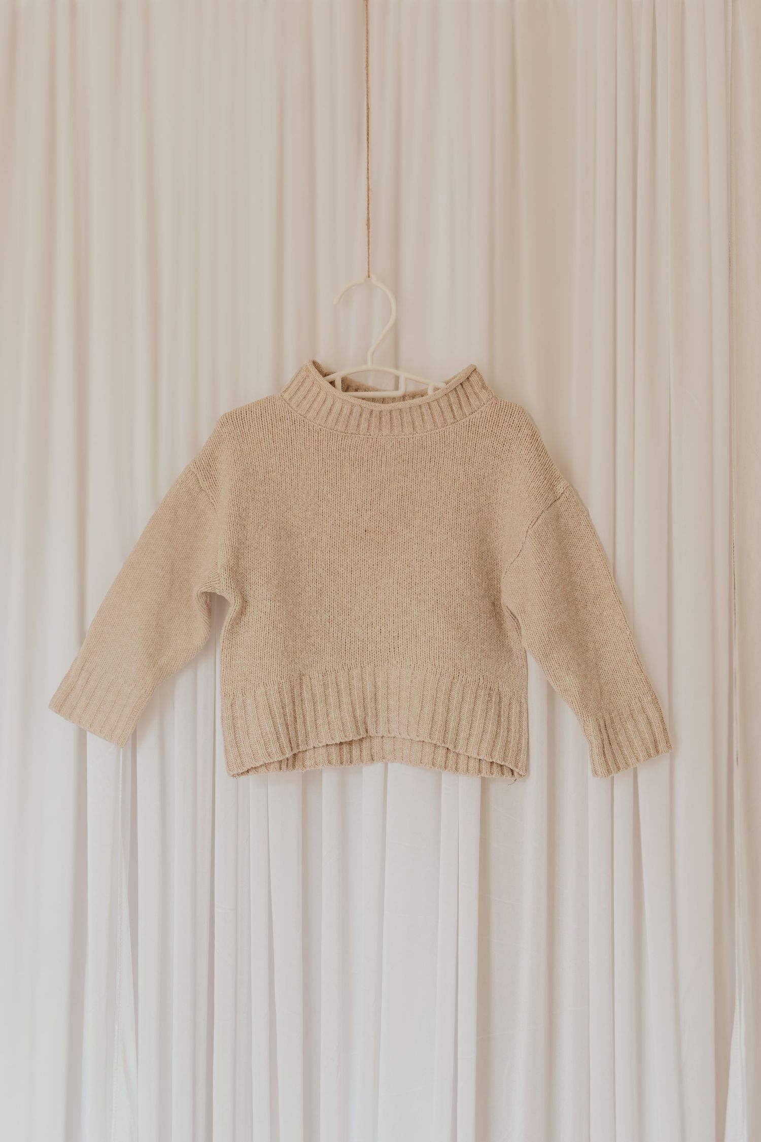 Beige Strickpullover, die an einem weißen Wanddisplay hängen und verschiedene Stile von neutral gefärbten Strickwaren zeigen.