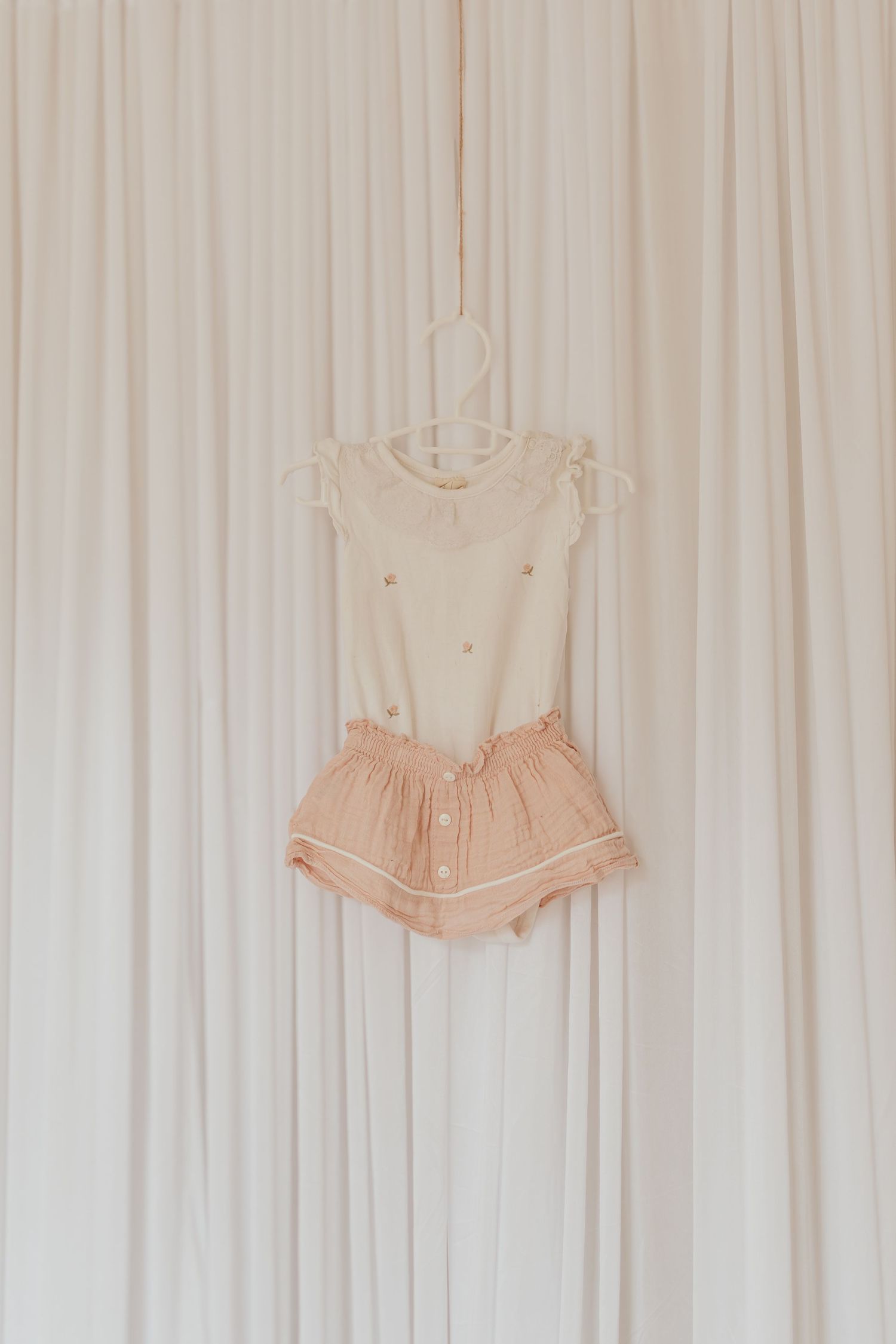 Abiti rosa per bambini in stile vintage appesi a tende bianche mostrano delicati dettagli femminili e volant.