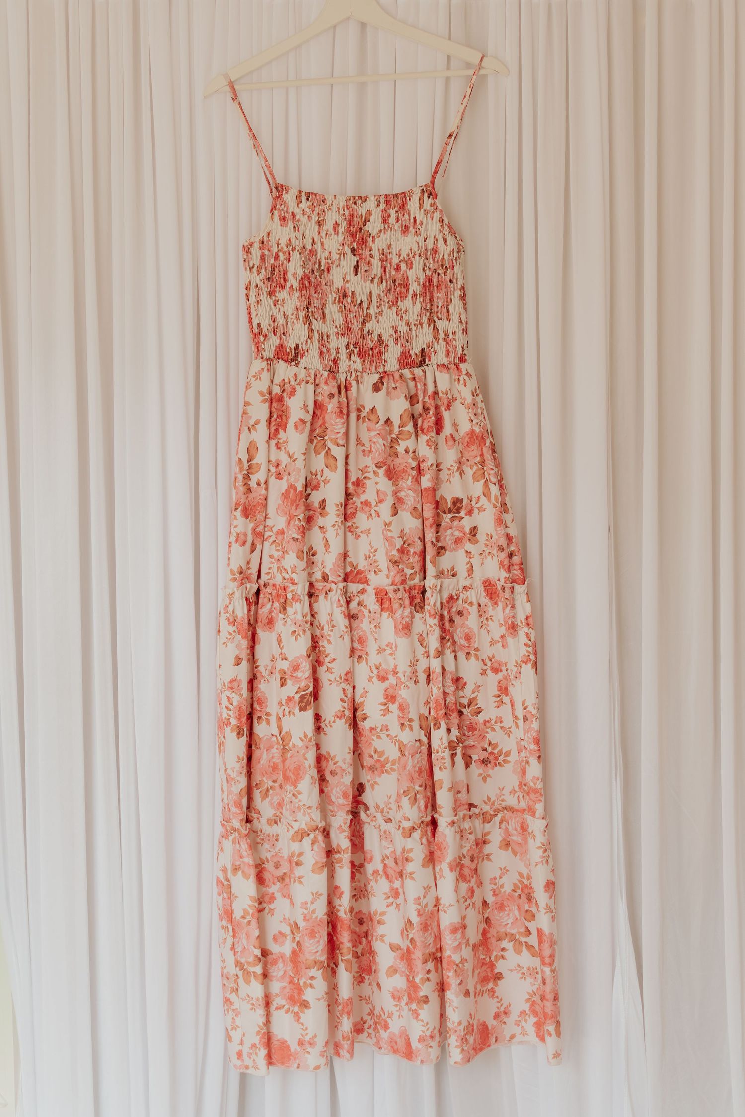 Rosa florales Sommerkleid, das an weißen Kleiderbügeln vor einem weißen Vorhanghintergrund hängt, zeigt eine romantische Sommerkollektion.