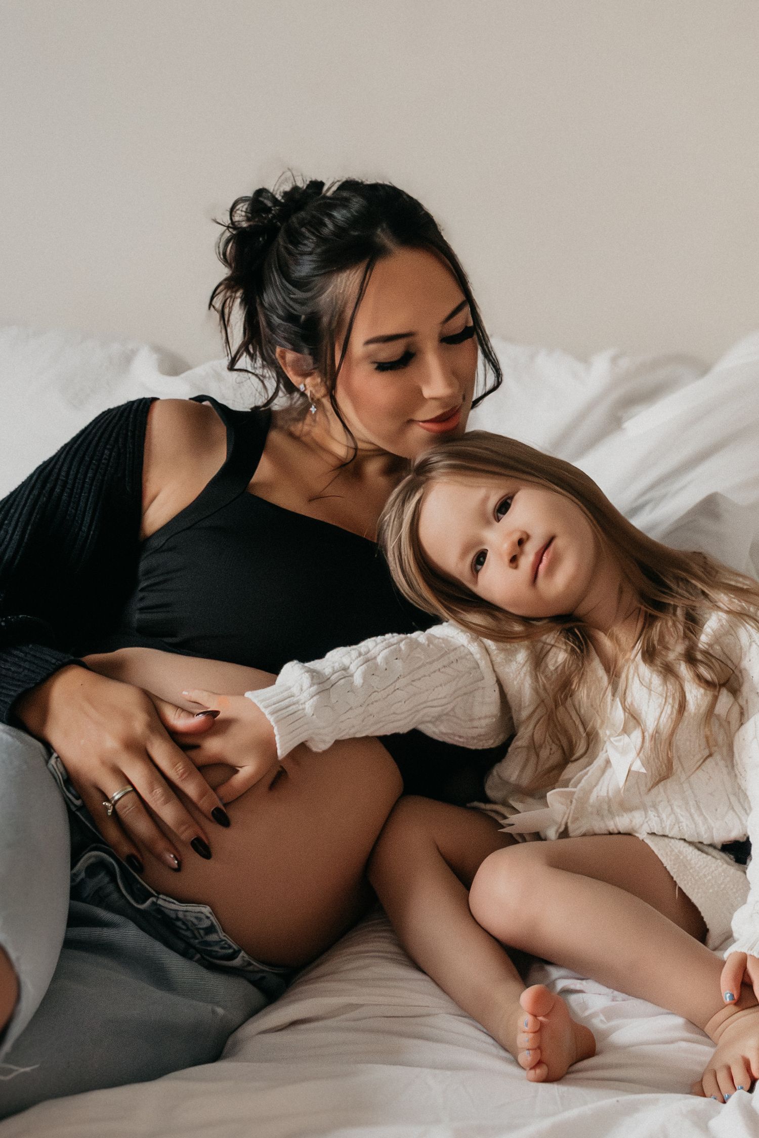 Intime Familienmomente zwischen werdender Mutter und Tochter, die in Schwarz und Weiß im Bett festgehalten werden.