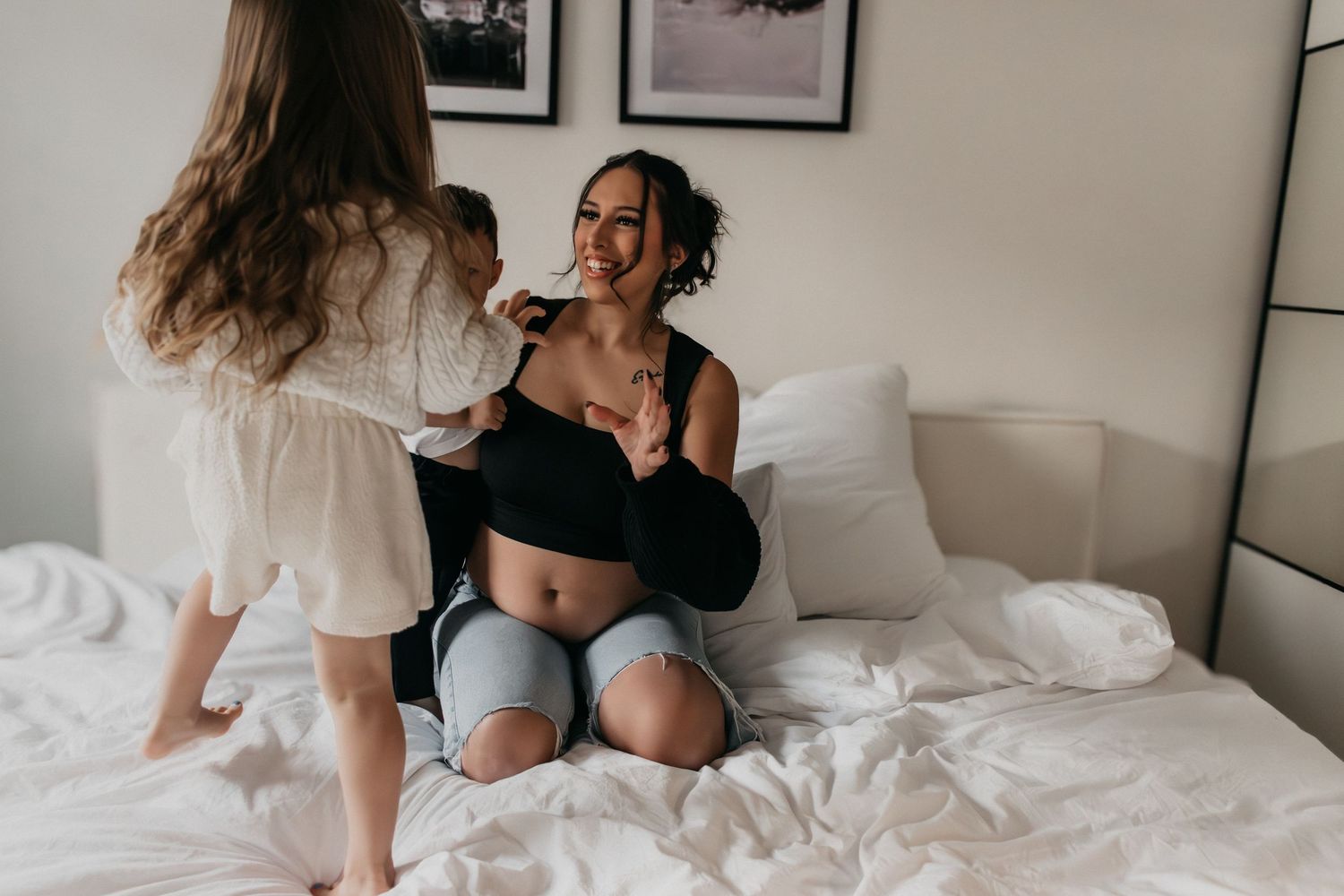 Familie entspannt sich zusammen auf weißer Bettwäsche mit gerahmten Fotos im Hintergrund.