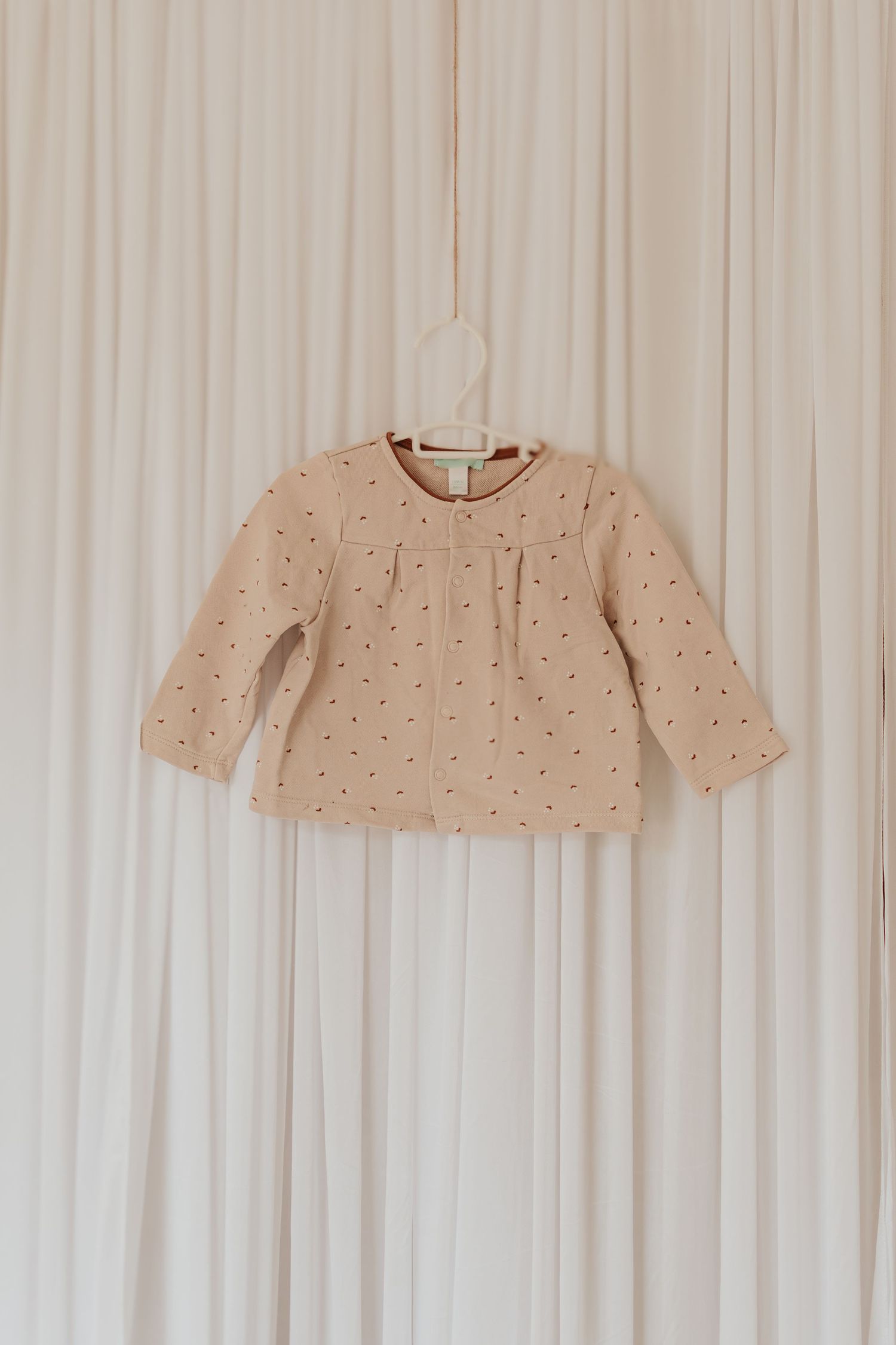 Beige gepunktete Pullover hängen an weißem Vorhang Hintergrund zeigen Kleidung Mode Merchandise.