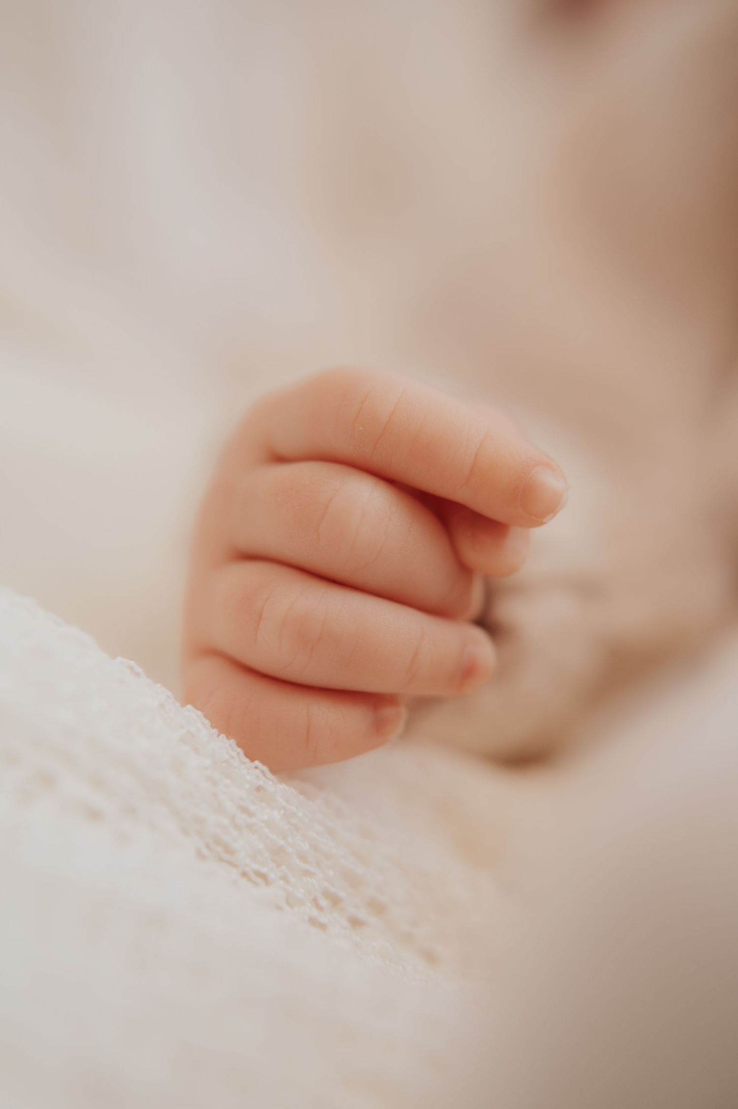 Close-up of a newborn baby's tiny delicate hand resting on a soft white knit blanket.