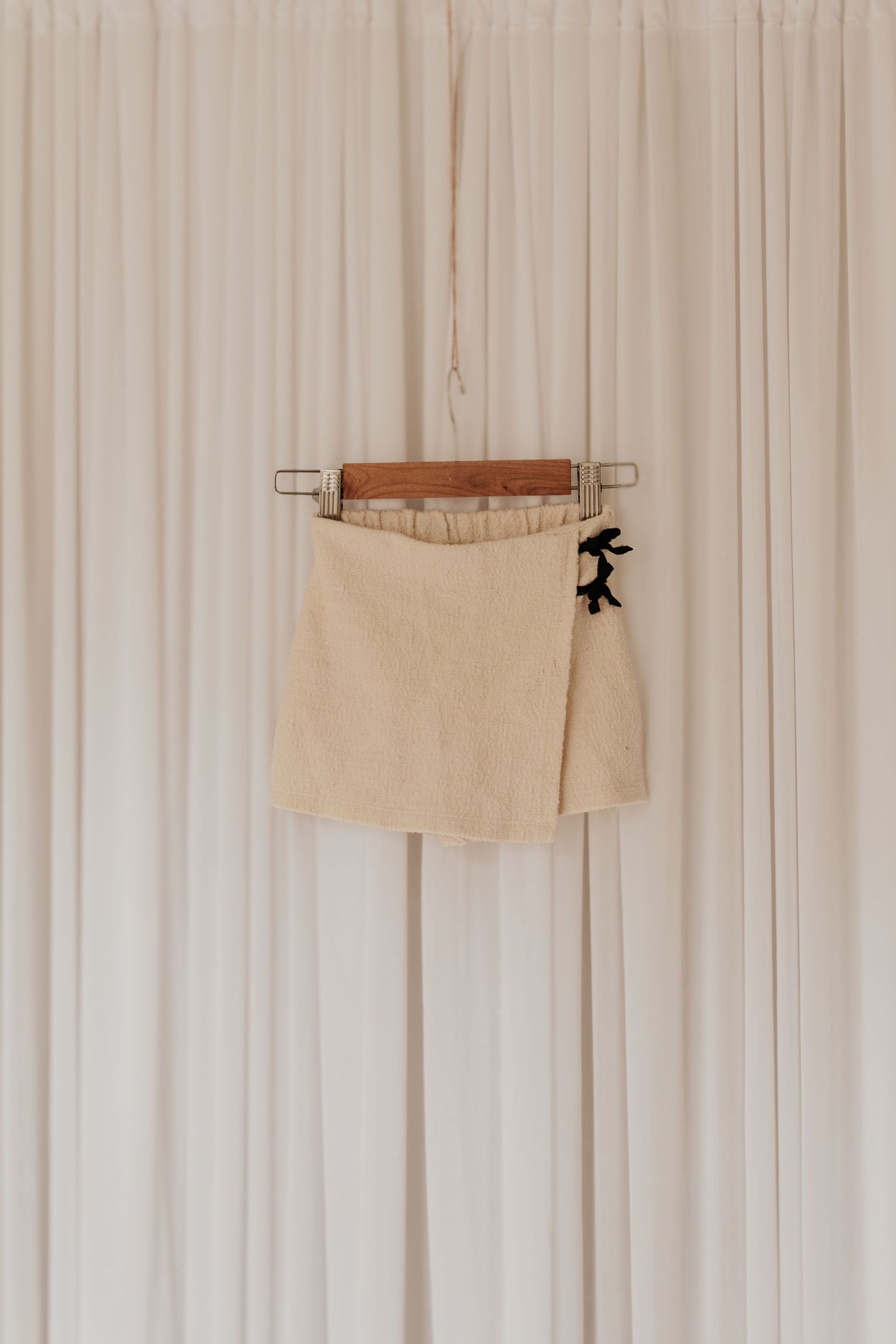 Cremefarbene Leinenshorts, die an hölzernen, an der Wand befestigten Haken an einer weißen Vorhangwand hängen.