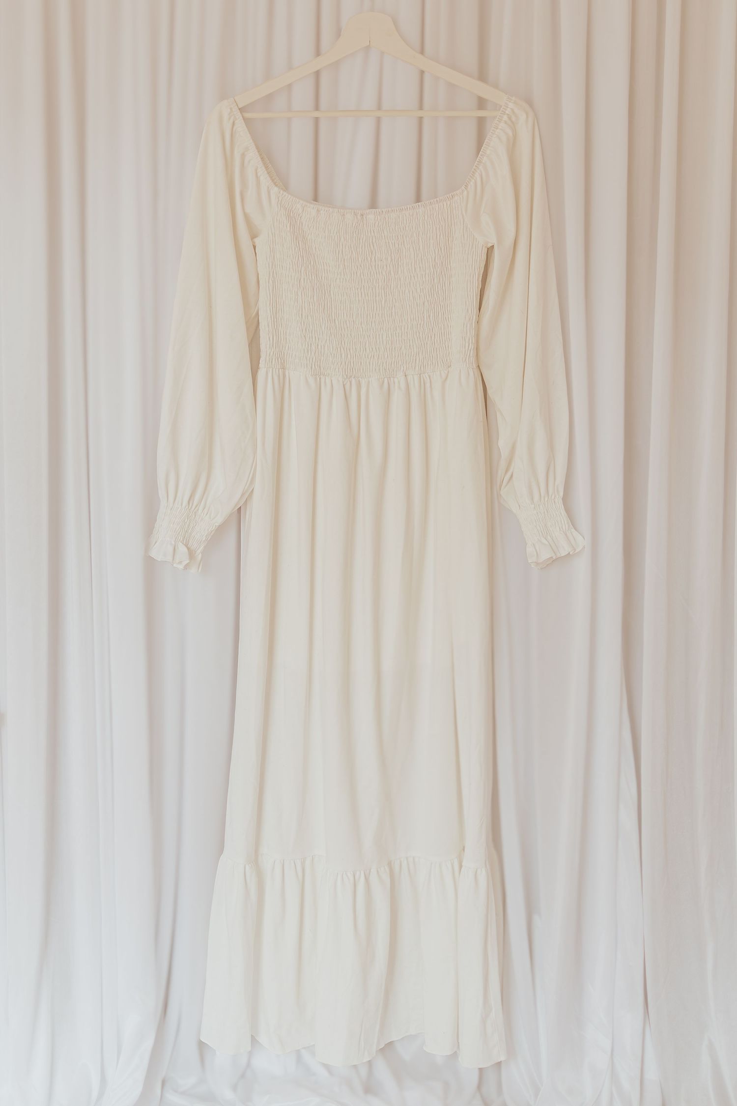 Elegante weiße Baumwollkleider mit langen Ärmeln, die auf einem weißen Vorhanghintergrund hängen.