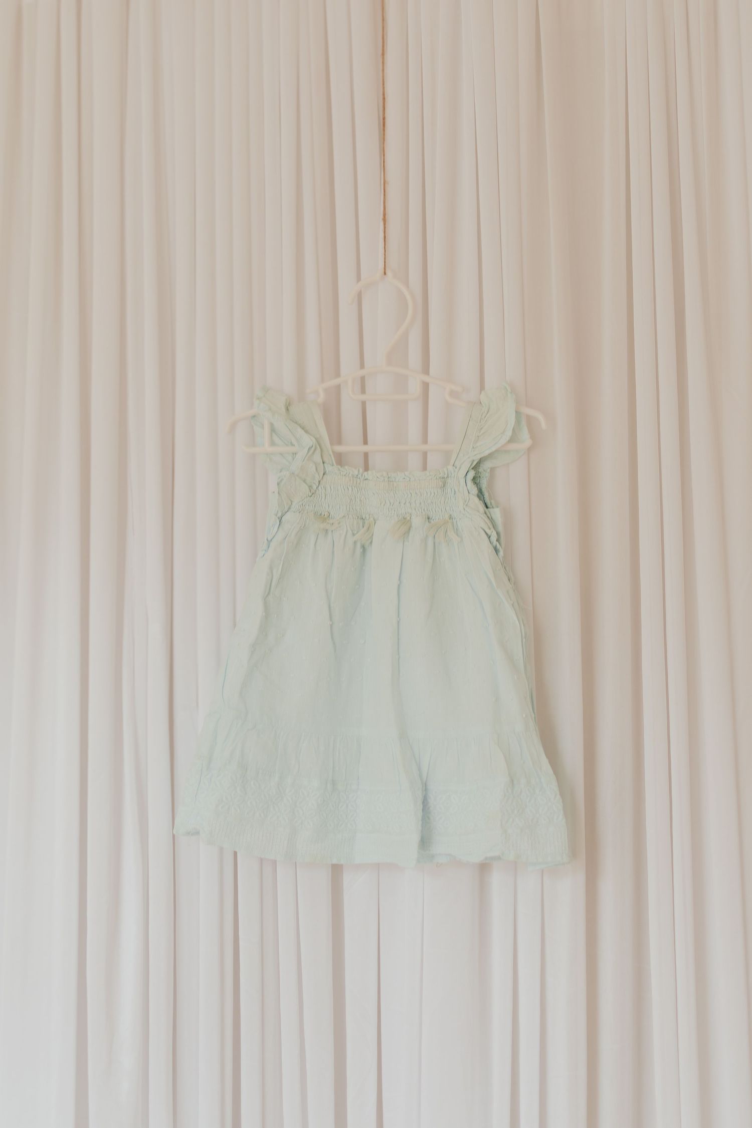 Hellblaues Kleid, das auf einem weißen Vorhanghintergrund in einer Reihe hängt.