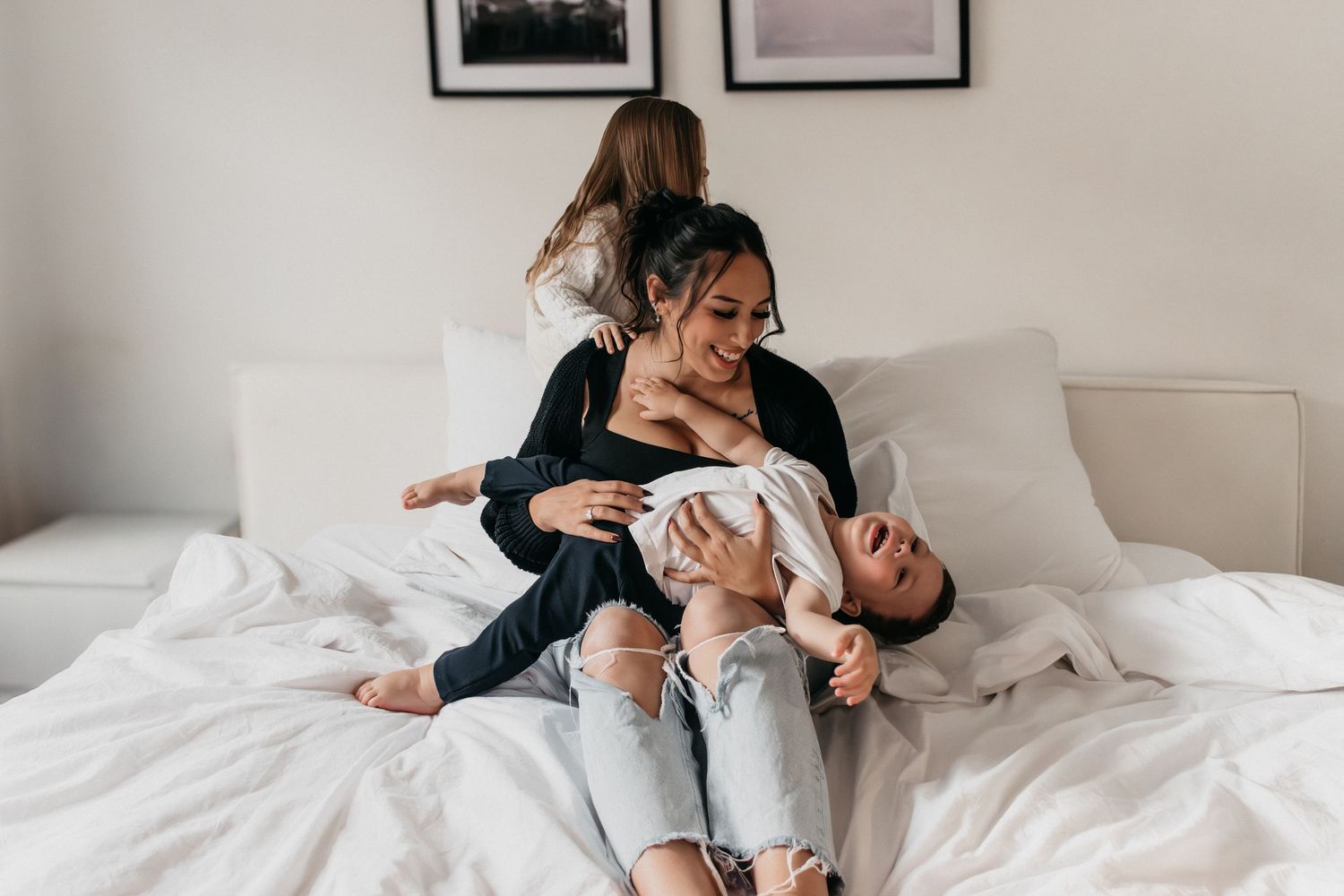Lifestyle-Fotografie-Session, die spielerische Familieninteraktionen auf weißer Bettwäsche zeigt.