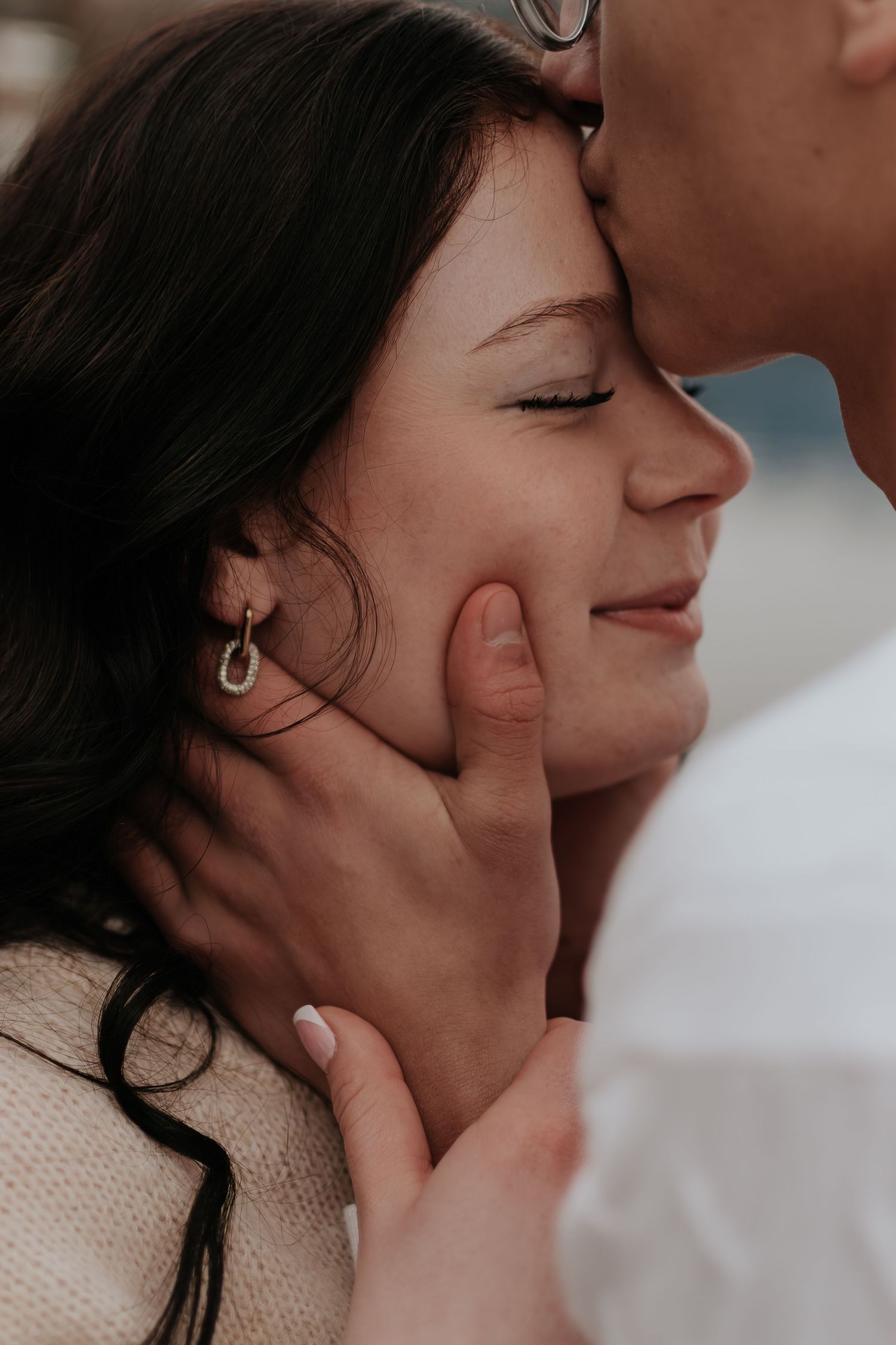 A man tenderly kisses a smiling woman's forehead while gently cupping her face in a romantic close-up.
