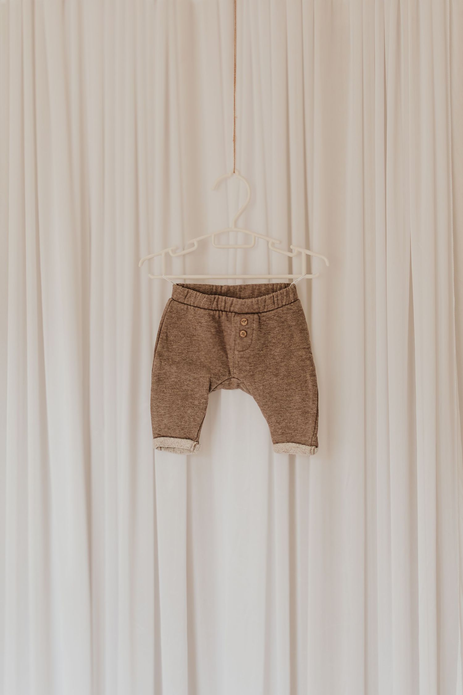 Paar braune Cordshorts, die an einem weißen Vorhang hängen.