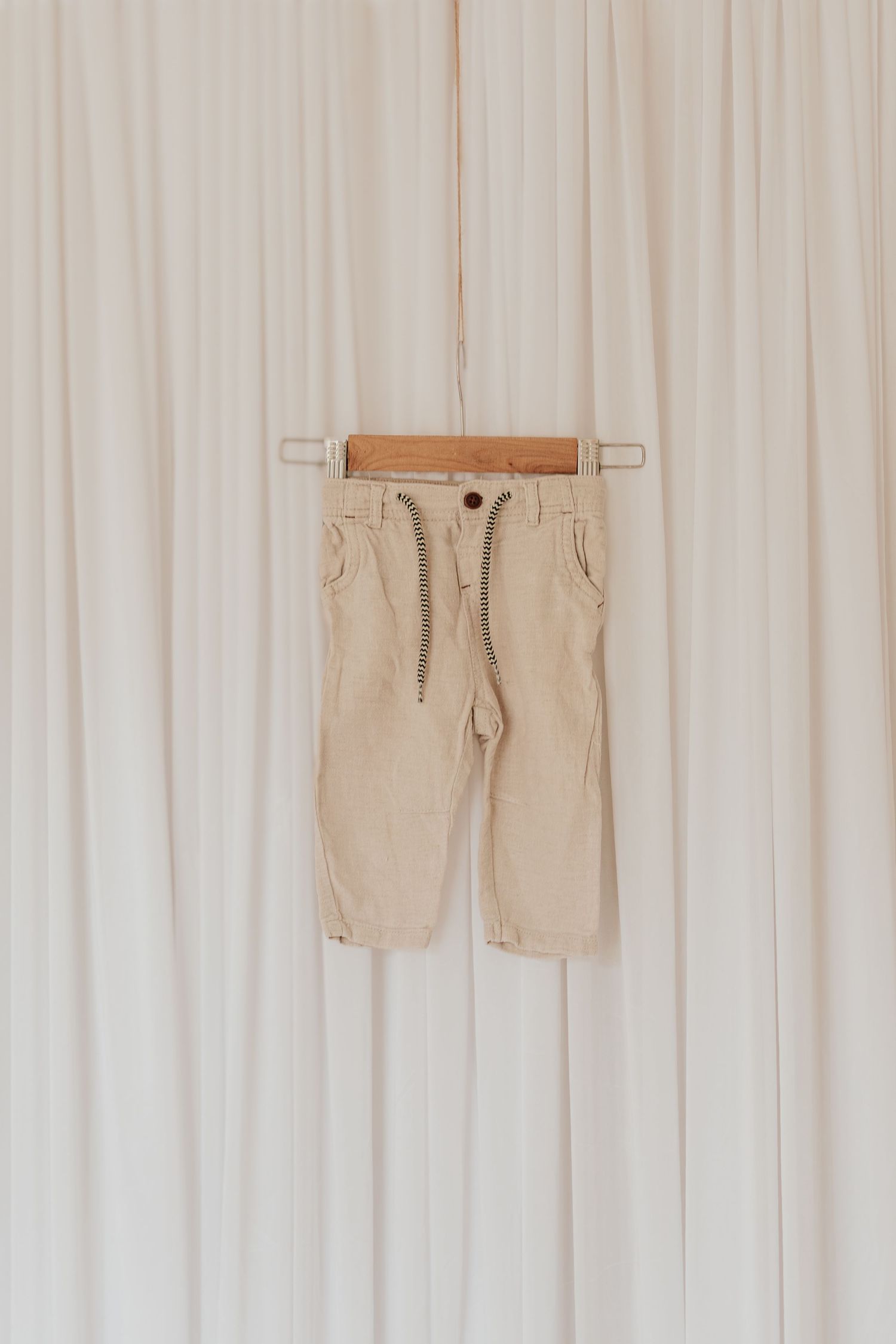 Beige khaki shorts hanging on white wooden wall hooks display casual summer wardrobe organization.