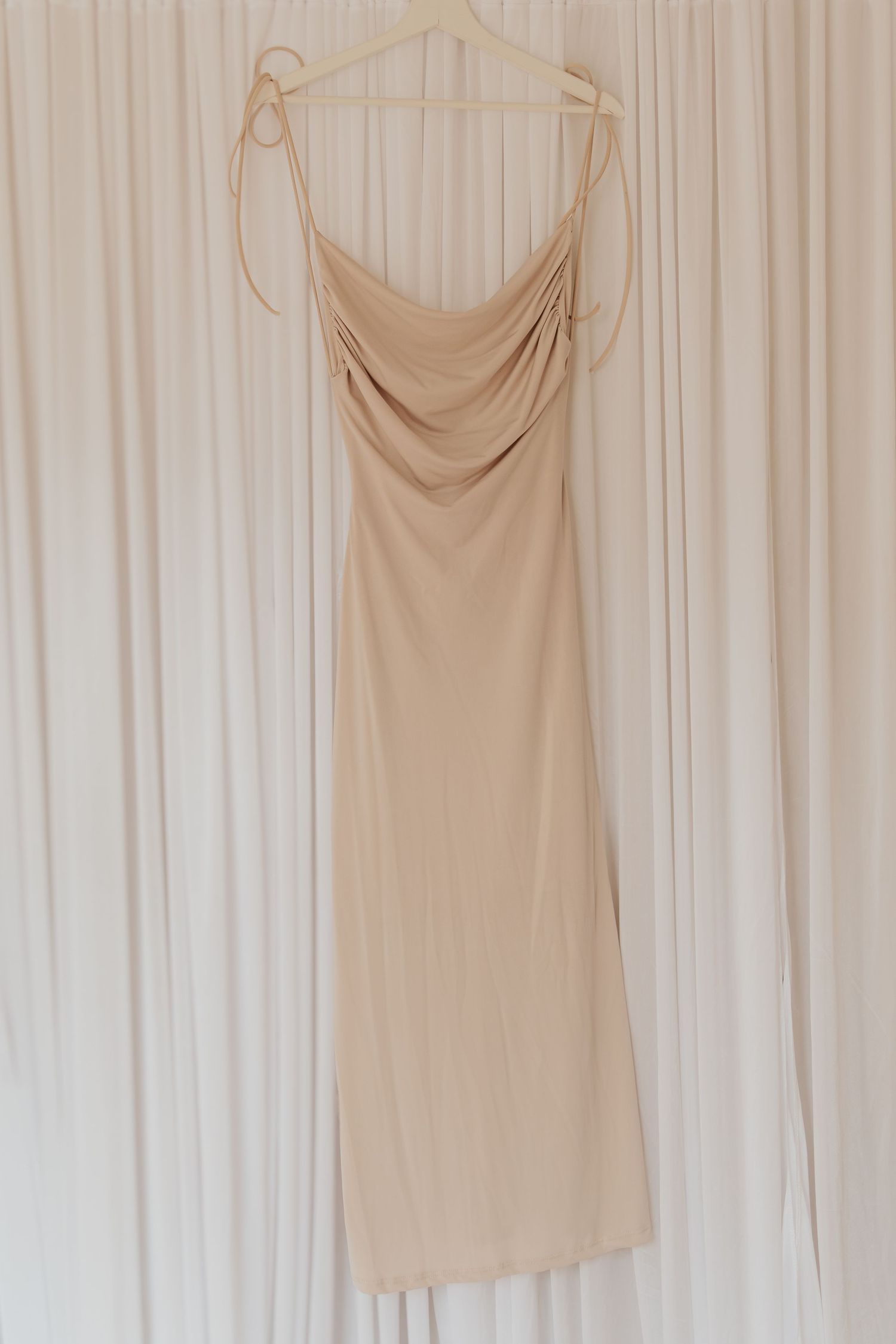 Beige ärmellose Tanktops, die an weißen Kleiderbügeln an einer hellen Wand hängen.