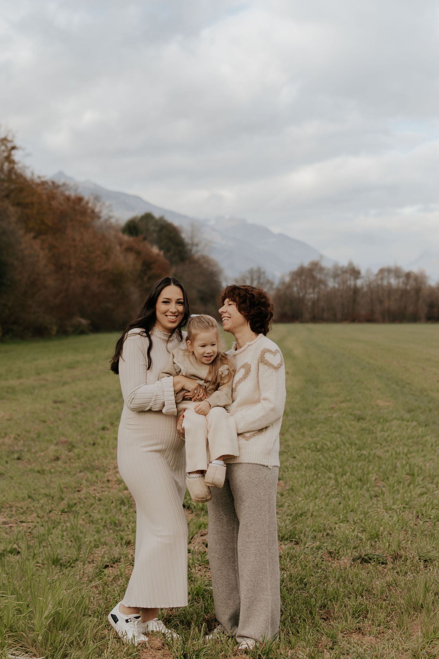Eine Familie teilt liebevolle Momente zusammen auf einem Feld mit Bergen im Hintergrund.
