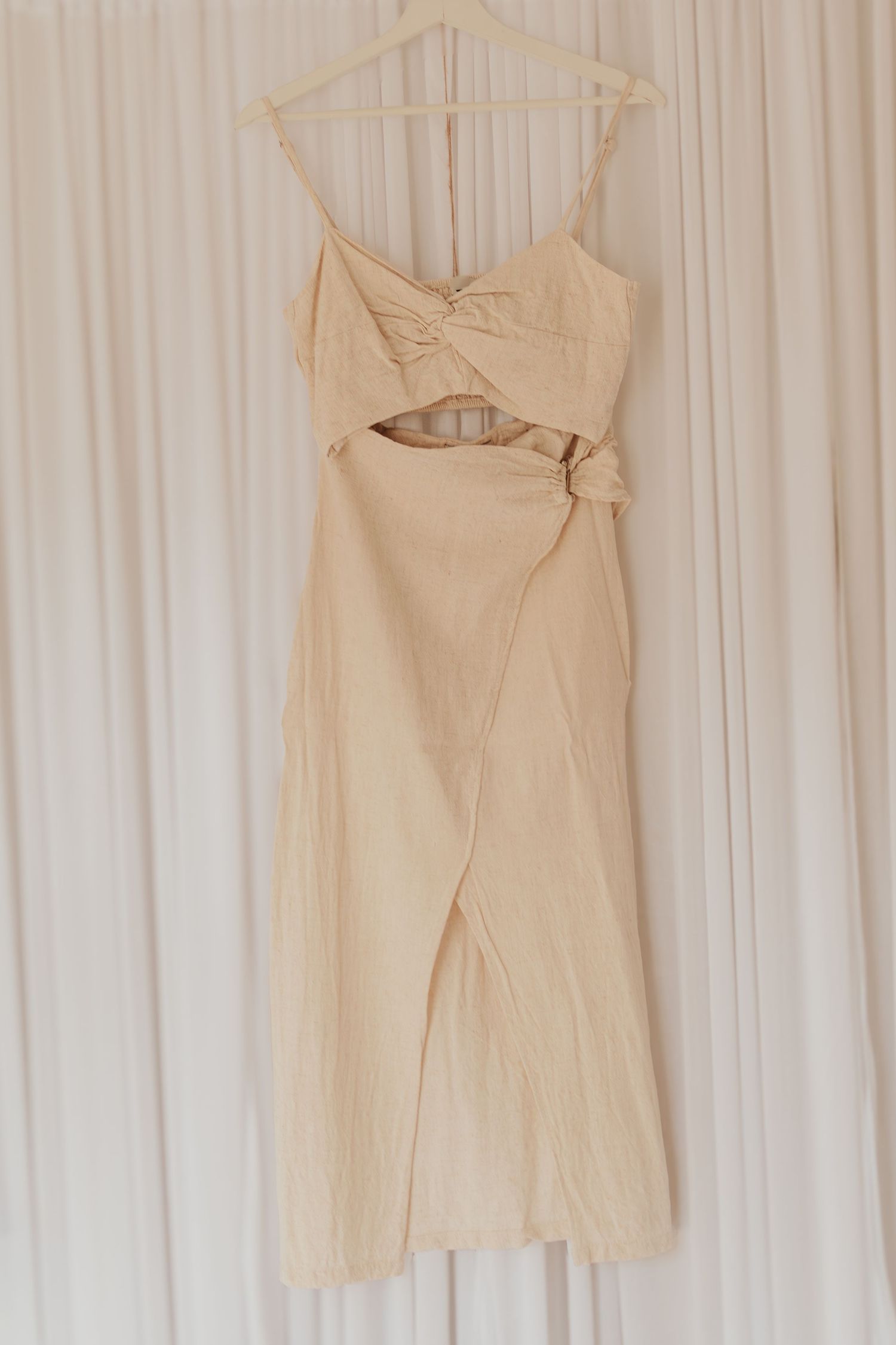 Beige 2-teiliges Kleid, das an weißen Vorhängen vor einem Wanddisplay hängt.