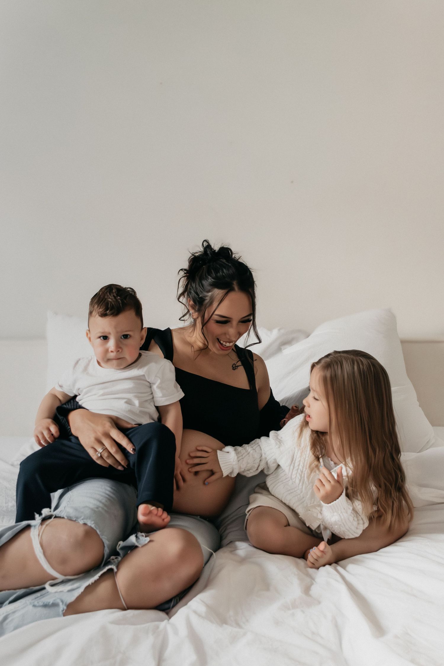 Die Familie kuschelt zusammen auf weißer Bettwäsche, während sie während des Lifestyle-Fotoshootings intime Momente teilt.
