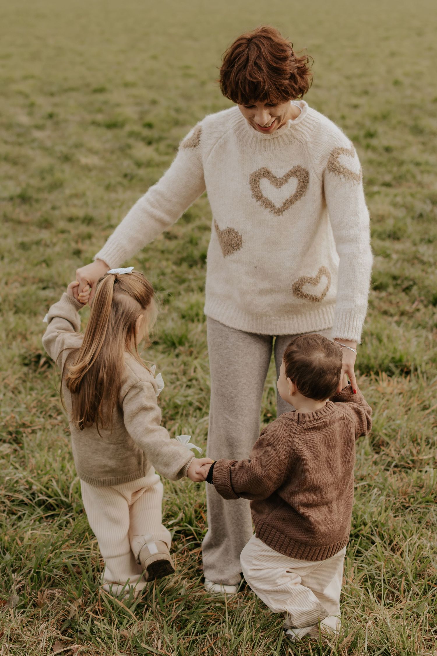 Spielerische Interaktion zwischen Kindern und Oma, die passende cremefarbene Pullover auf dem Rasen tragen.