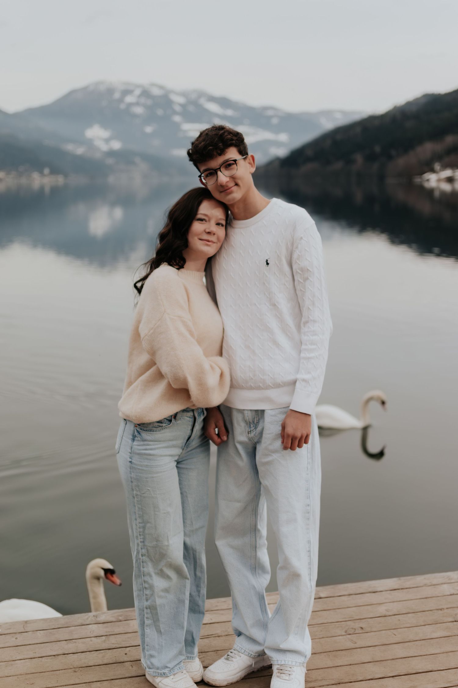 Paar in hellen Outfits, das auf einem Holzdock am Nebelsee steht.