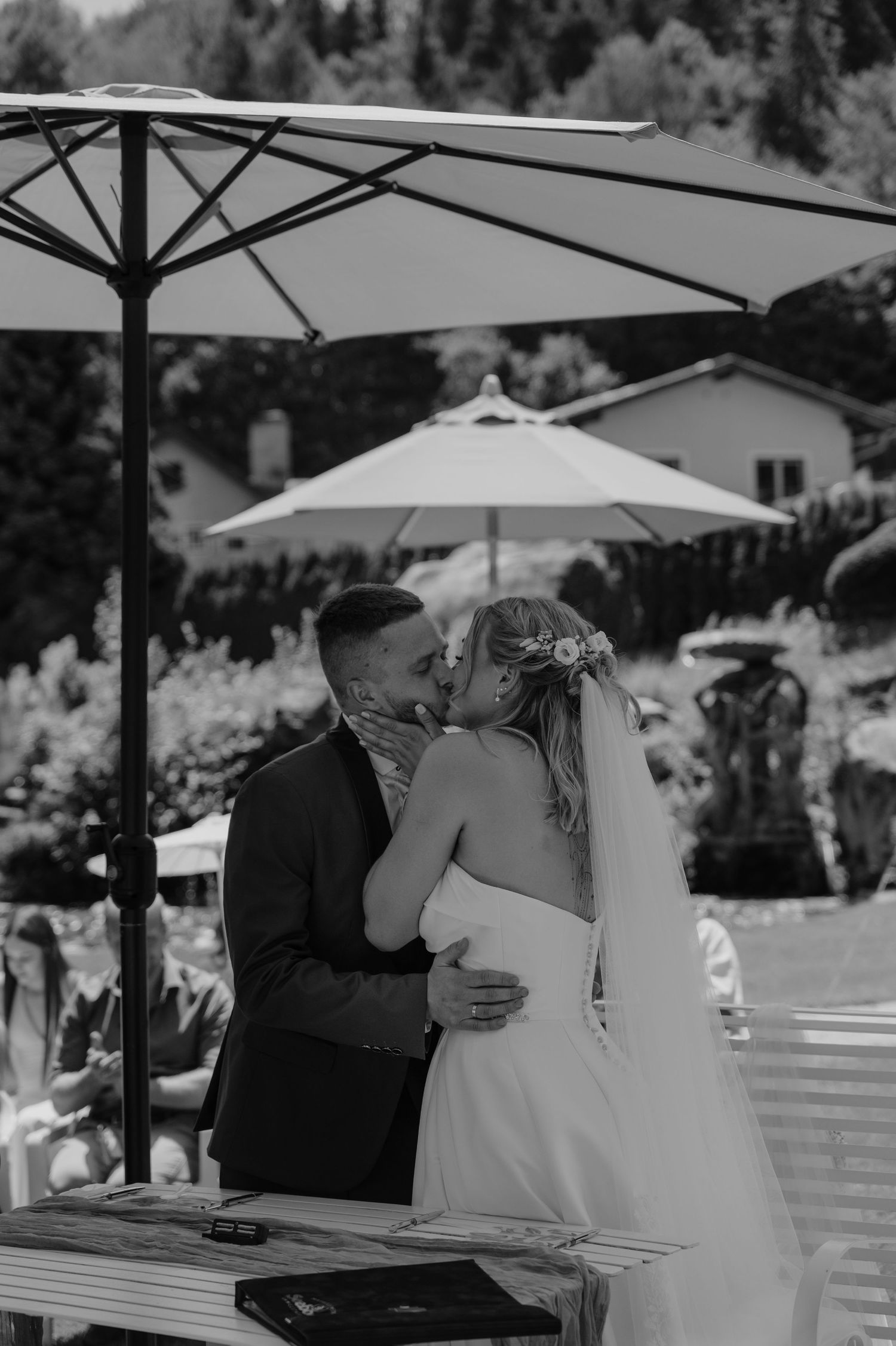 Black and white photo of a bride and groom sharing their first kiss at an outdoor wedding ceremony.
