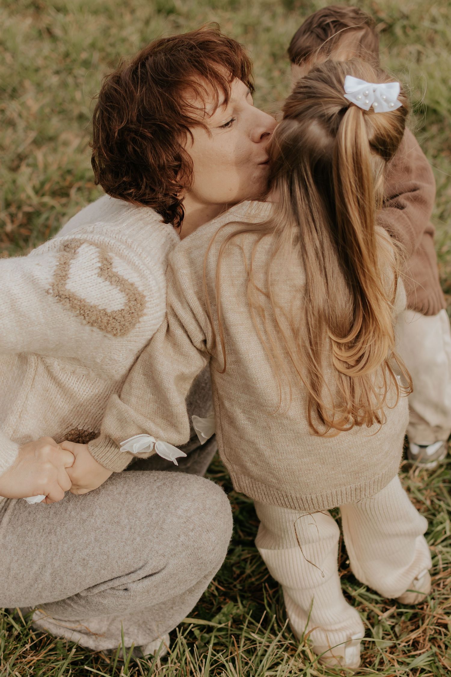 Ehrliche Familienfotografie, die zarte Momente in passenden neutralen Pullovern auf Gras zeigt.