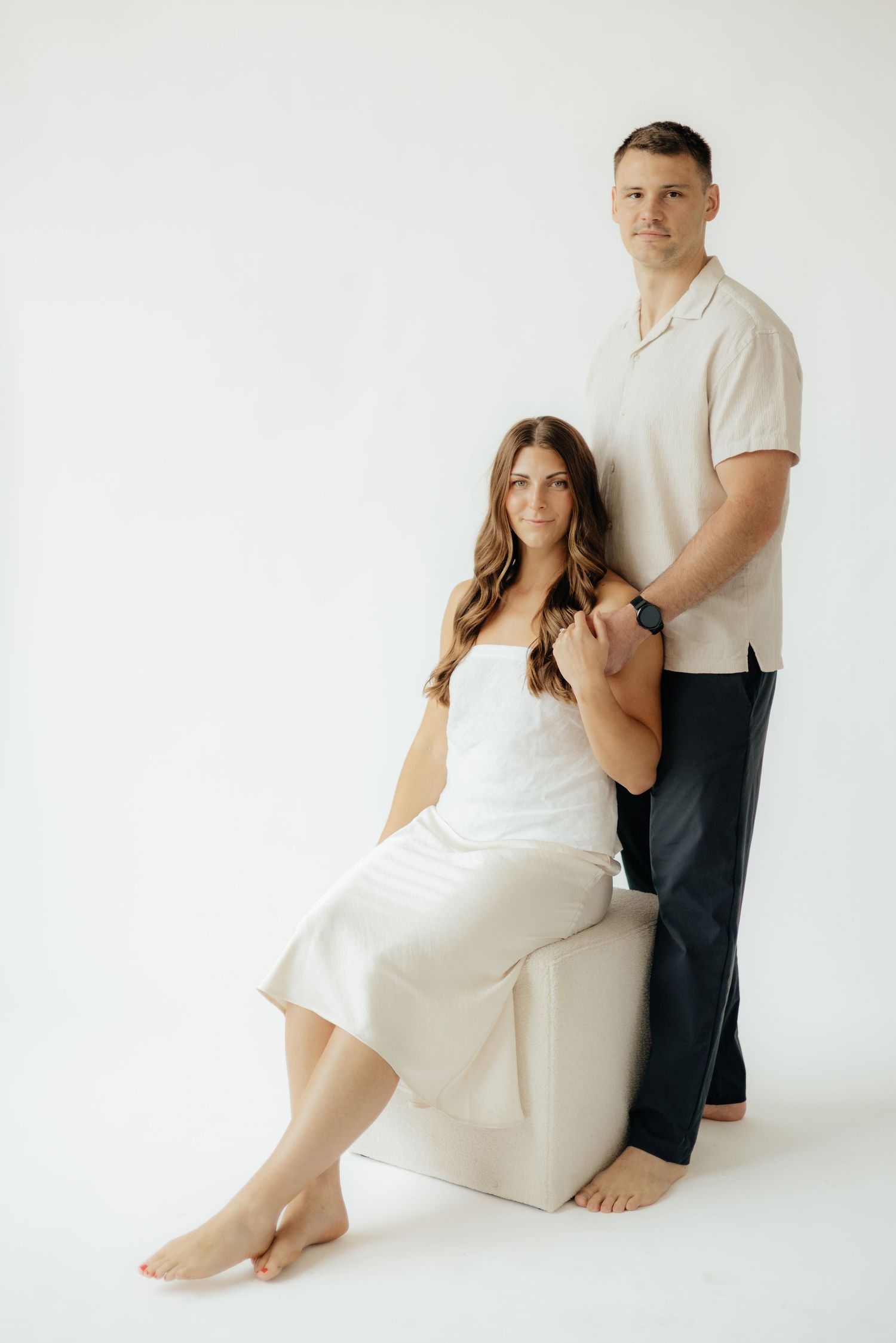 Couple embracing in soft natural light at Abide Studio in Minneapolis, MN, with minimalist white walls and warm, cozy tones
