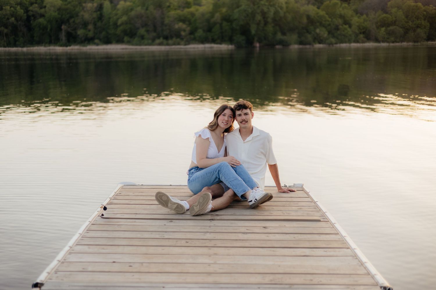 Couple smiling together along the lakeshore at Fish Lake Regional Park in Maple Grove, MN, with bright green trees and clear blue water