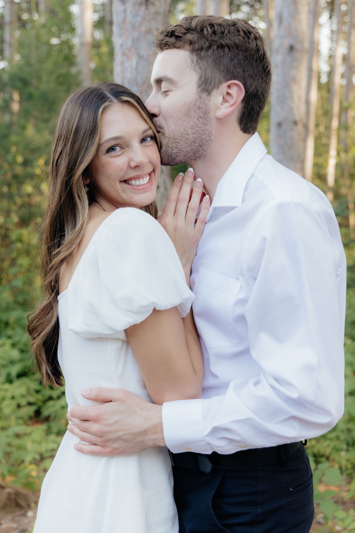 Golden-hour portrait of a couple embracing among tall trees at Pinewood in Cambridge, showcasing woodsy elegance.