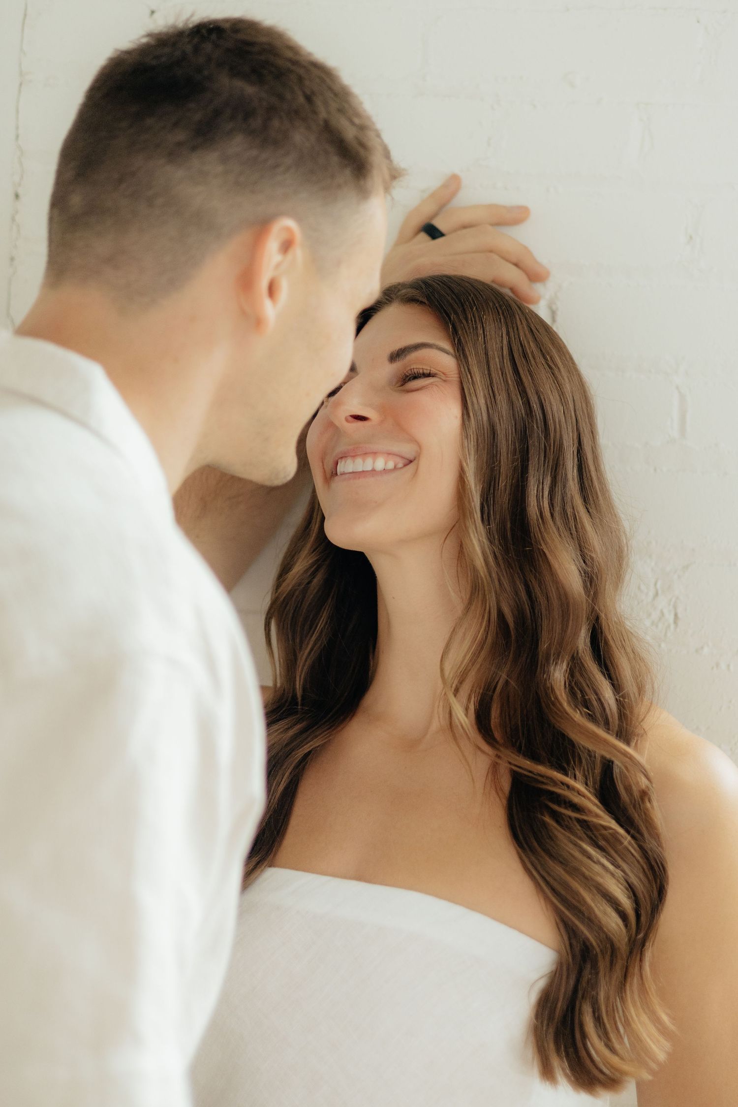 Couple embracing in soft natural light at Abide Studio in Minneapolis, MN, with minimalist white walls and warm, cozy tones