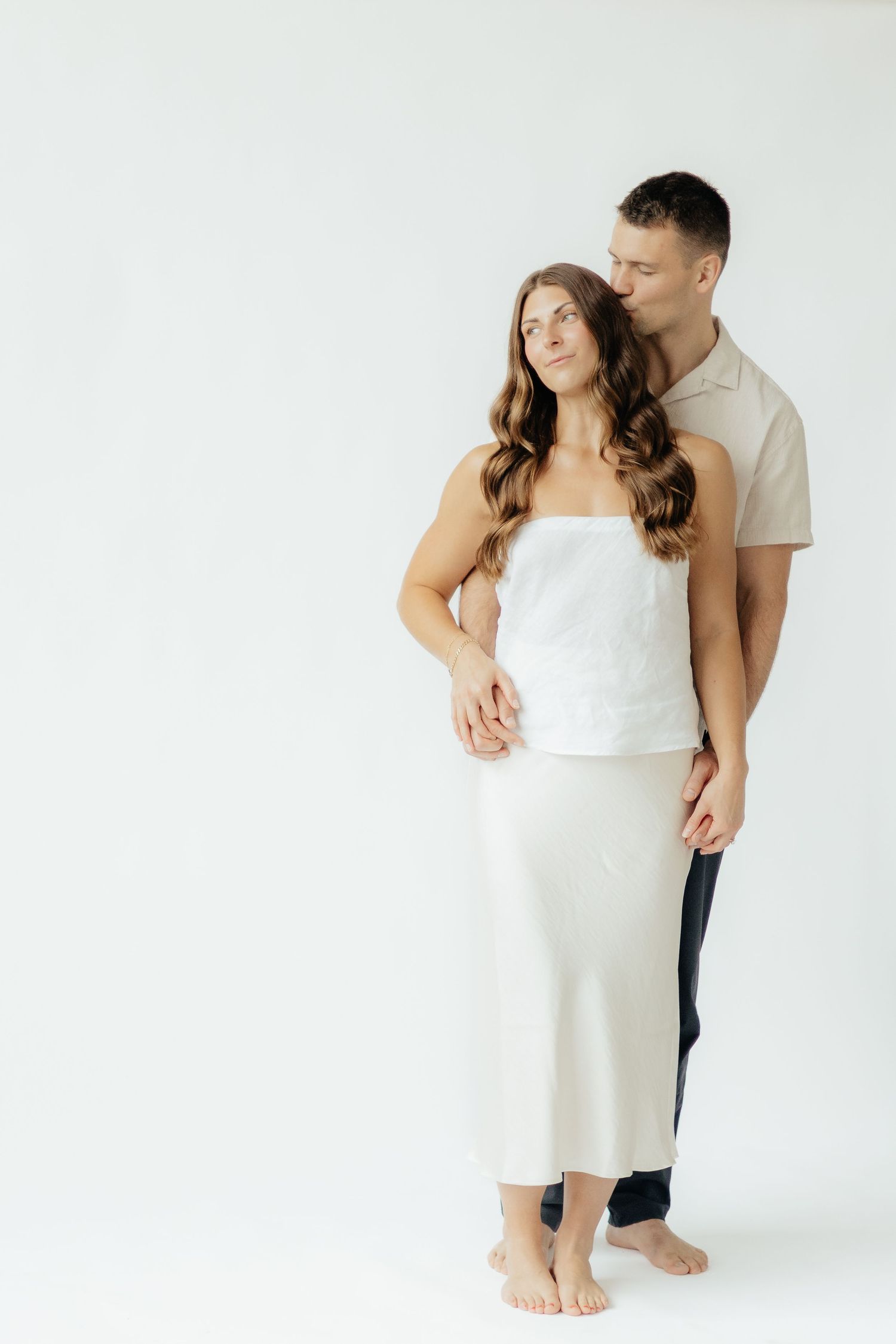 Couple embracing in soft natural light at Abide Studio in Minneapolis, MN, with minimalist white walls and warm, cozy tones