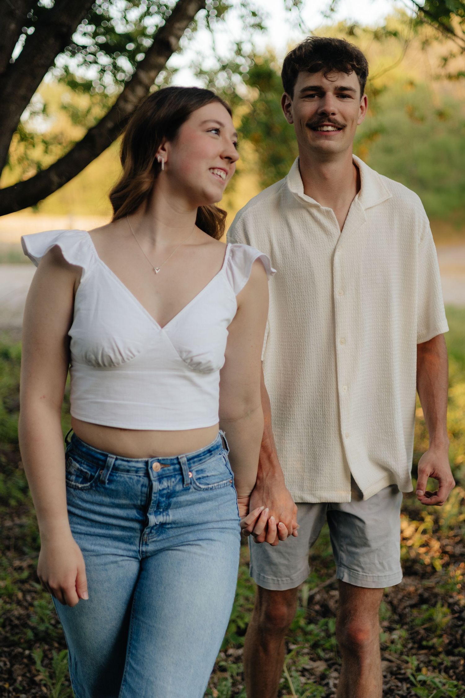 Couple smiling together along the lakeshore at Fish Lake Regional Park in Maple Grove, MN, with bright green trees and clear blue water