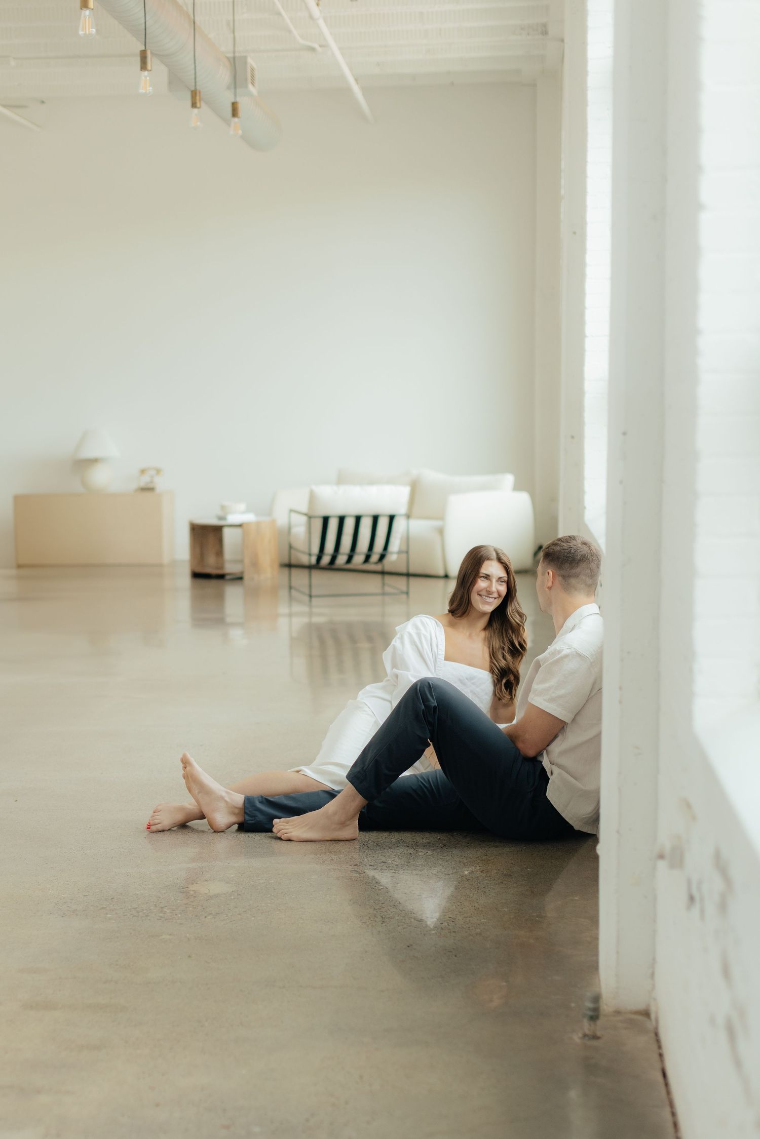 Couple embracing in soft natural light at Abide Studio in Minneapolis, MN, with minimalist white walls and warm, cozy tones