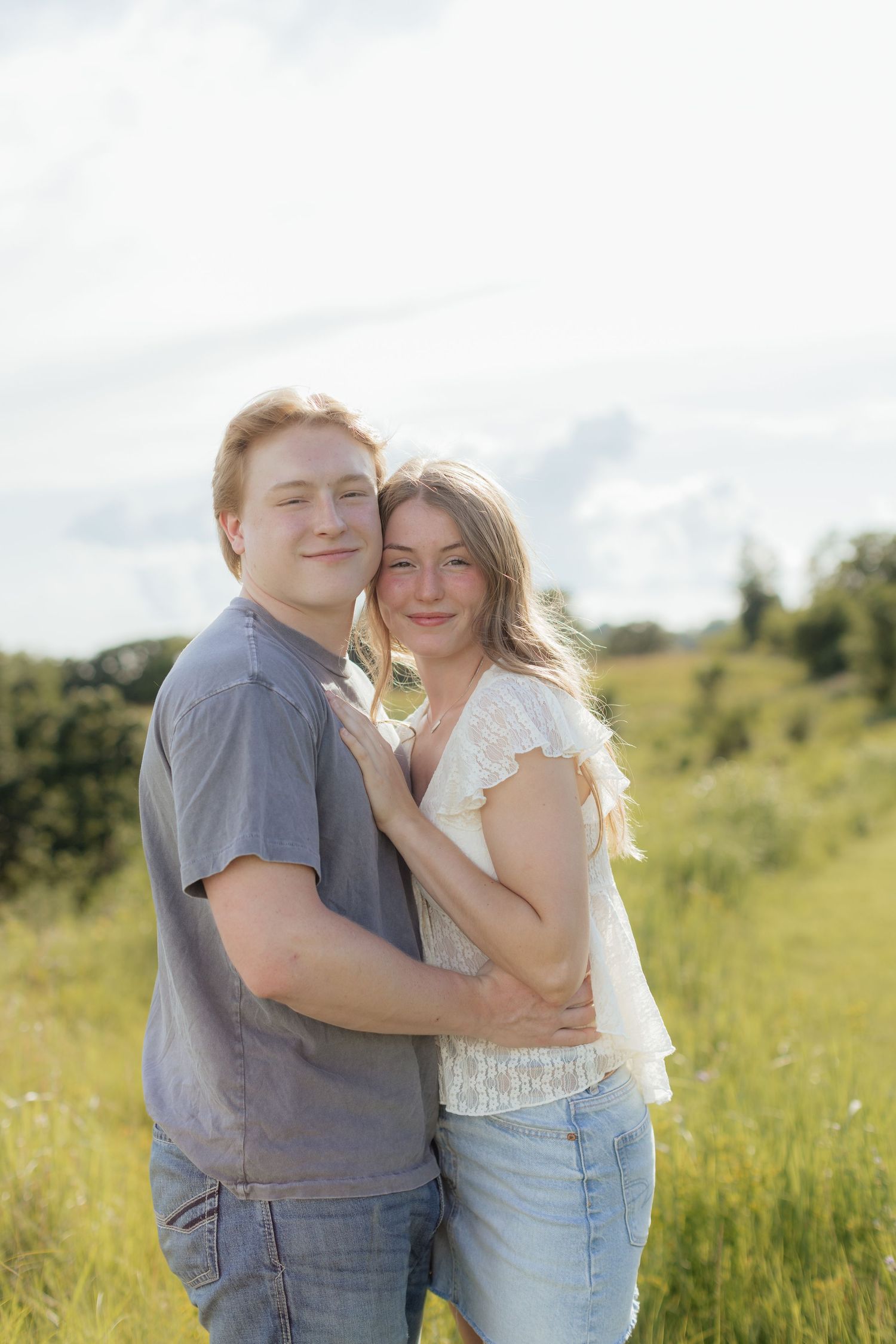 Romantic photo of a couple embracing on a hilltop at Prairie Bluffs, surrounded by open fields and wide Minnesota skies.