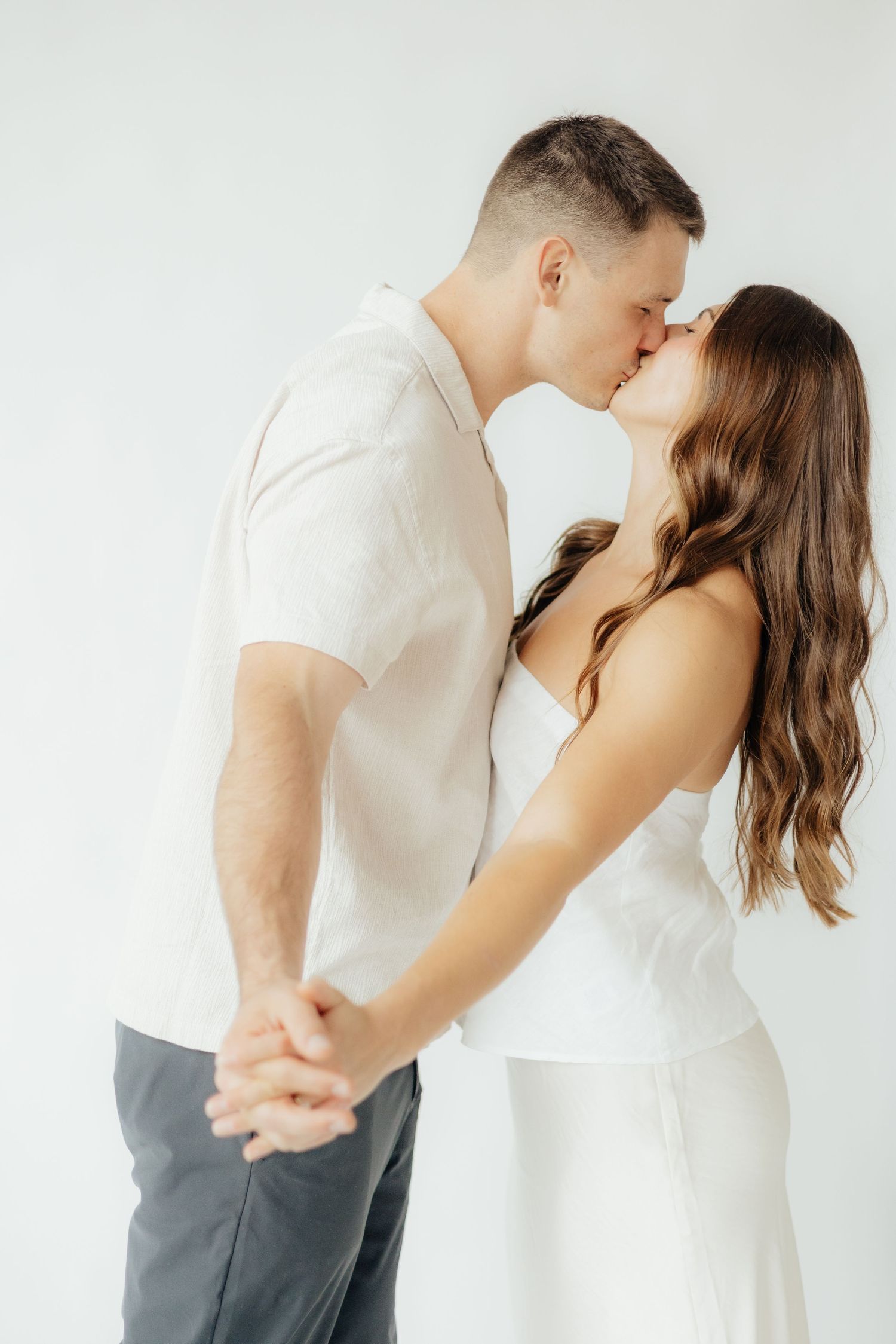 Couple embracing in soft natural light at Abide Studio in Minneapolis, MN, with minimalist white walls and warm, cozy tones