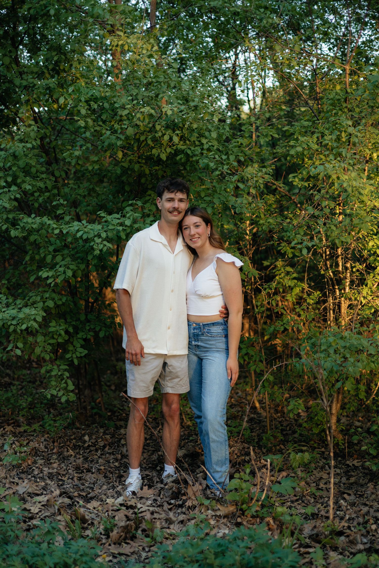 Couple smiling together along the lakeshore at Fish Lake Regional Park in Maple Grove, MN, with bright green trees and clear blue water