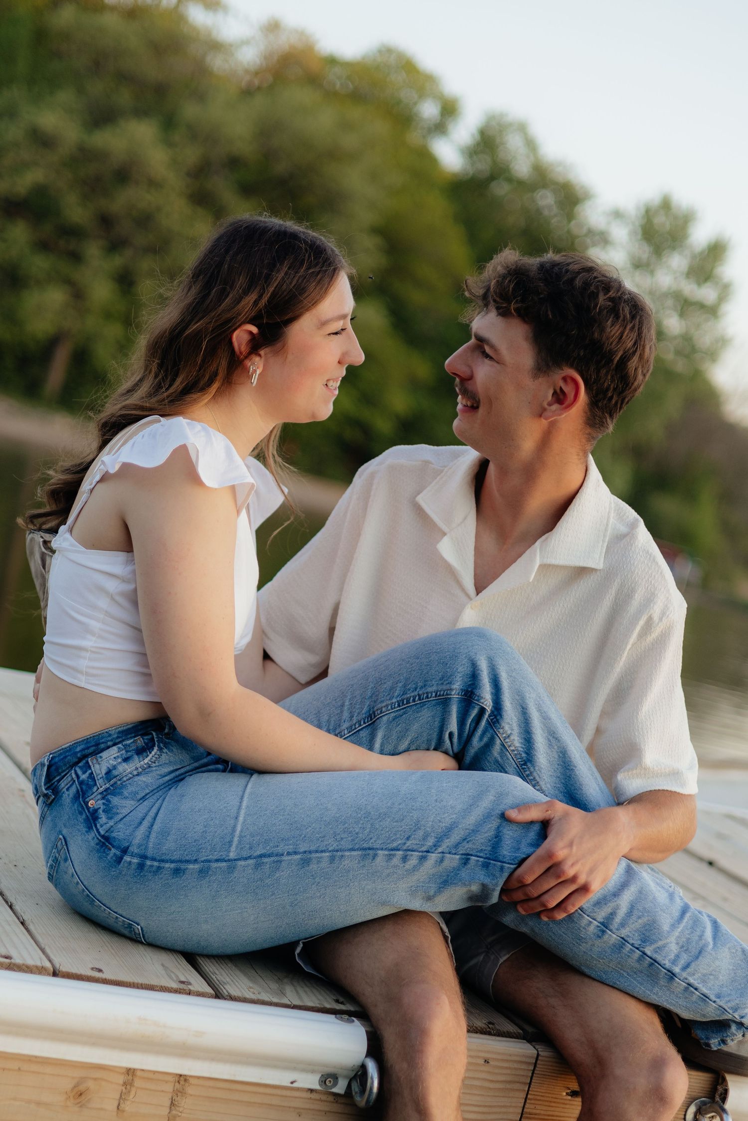 Couple smiling together along the lakeshore at Fish Lake Regional Park in Maple Grove, MN, with bright green trees, clear blue water