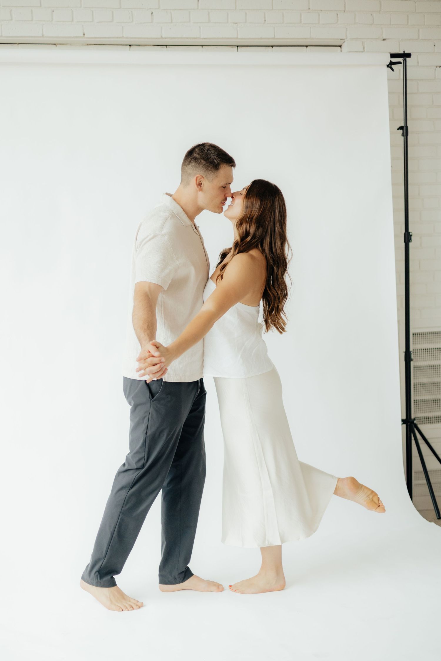 Couple embracing in soft natural light at Abide Studio in Minneapolis, MN, with minimalist white walls and warm, cozy tones