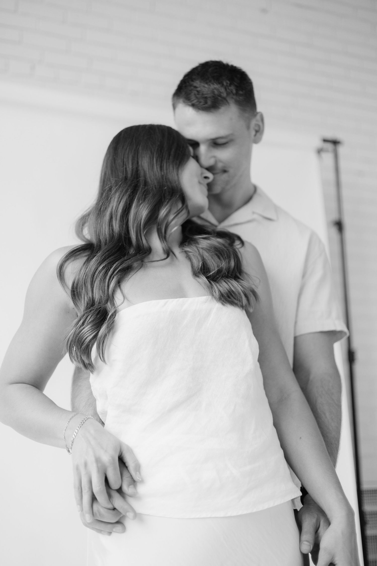 Couple embracing in soft natural light at Abide Studio in Minneapolis, MN, with minimalist white walls and warm, cozy tones