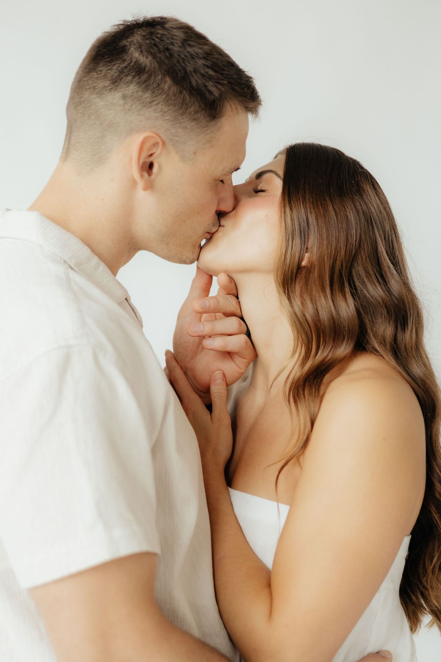 Couple embracing in soft natural light at Abide Studio in Minneapolis, MN, with minimalist white walls and warm, cozy tones