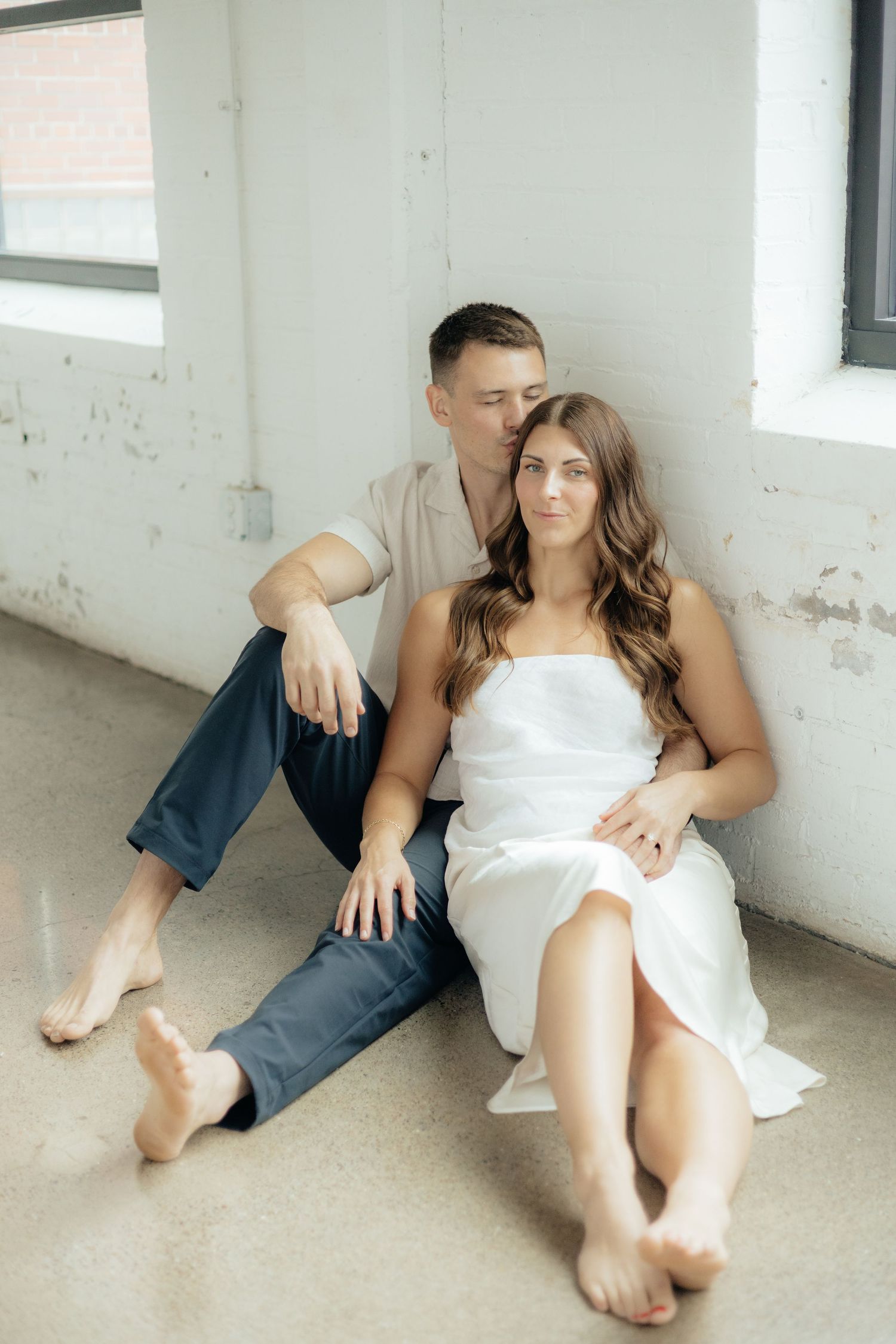 Couple embracing in soft natural light at Abide Studio in Minneapolis, MN, with minimalist white walls and warm, cozy tones
