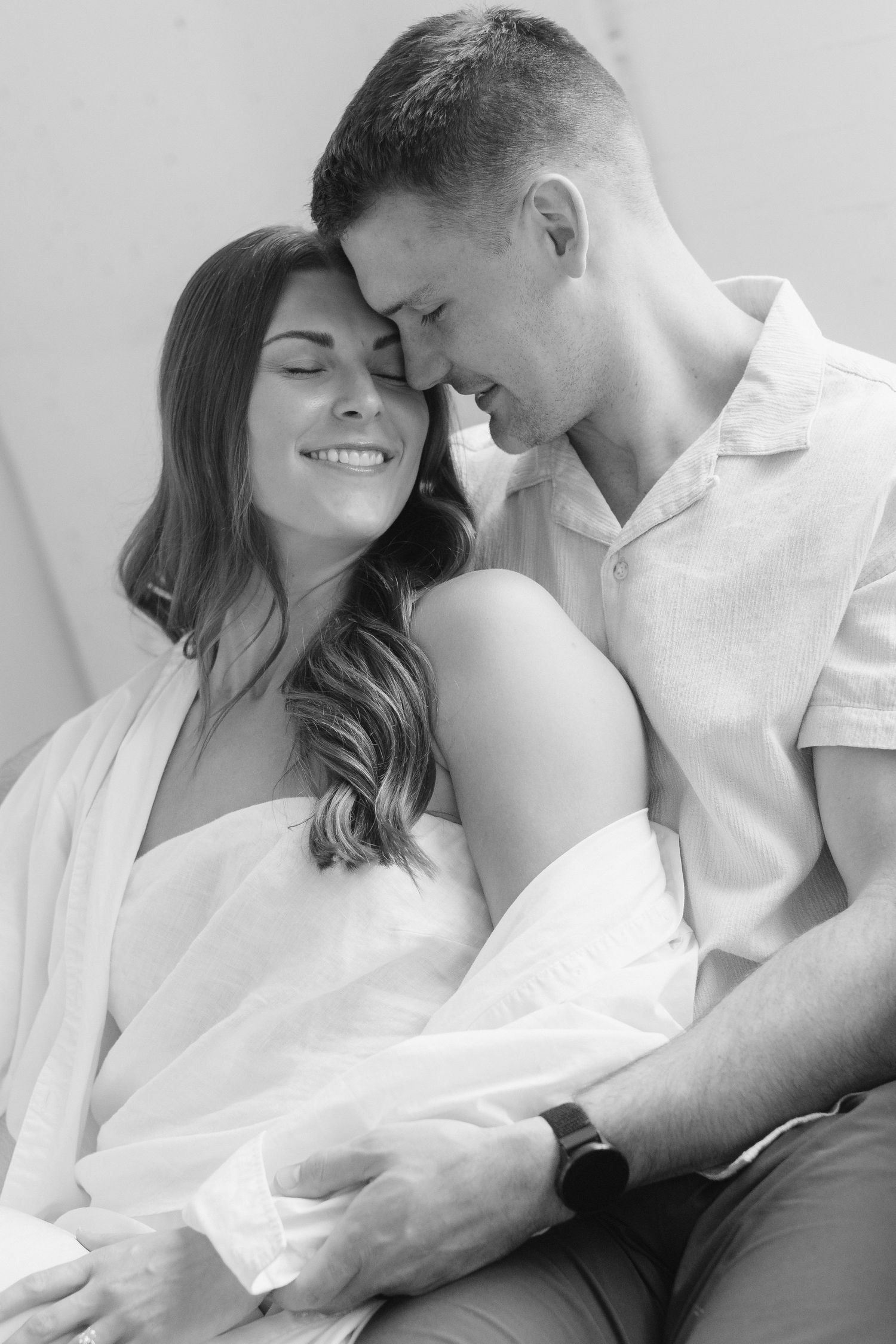 Couple embracing in soft natural light at Abide Studio in Minneapolis, MN, with minimalist white walls and warm, cozy tones
