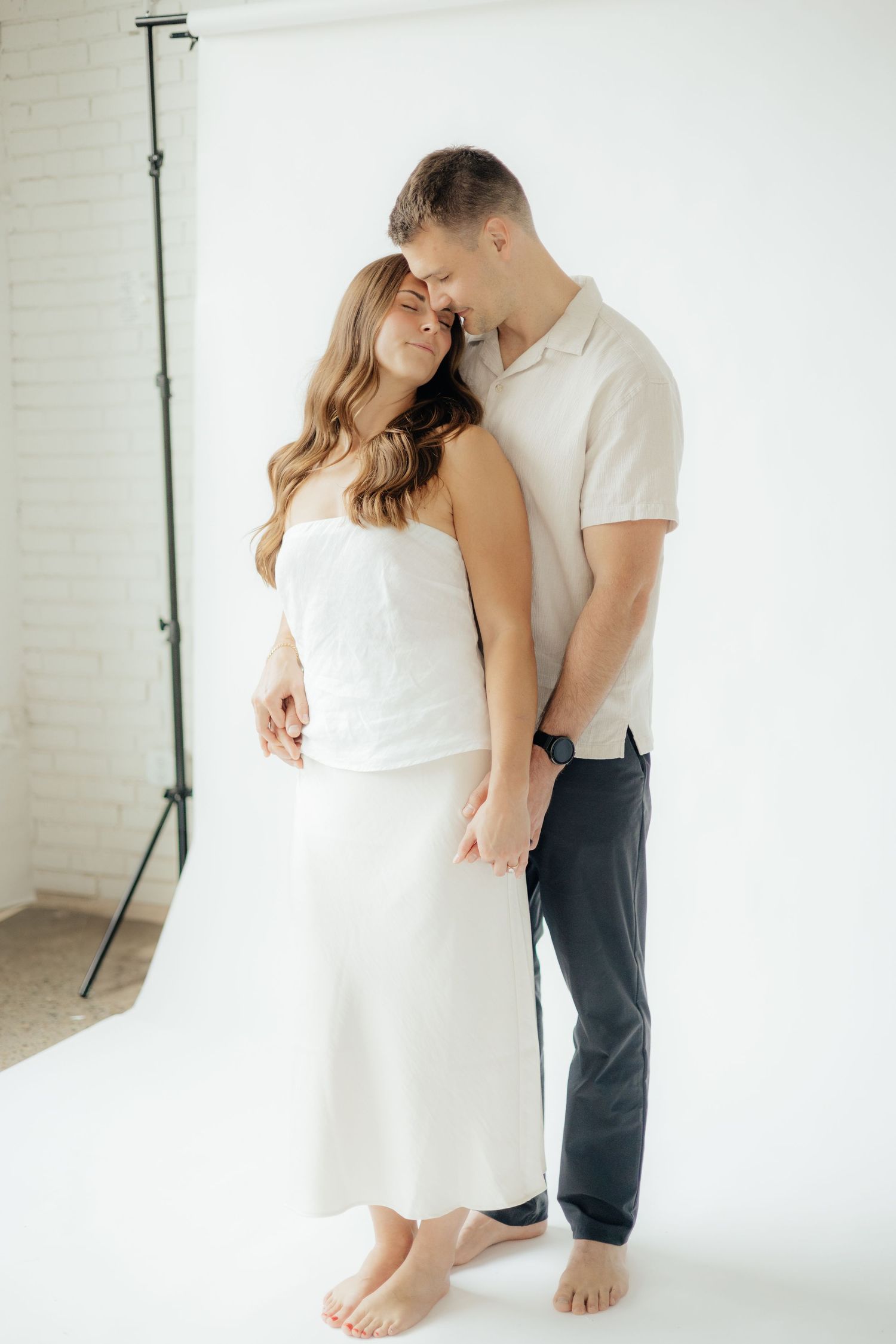 Couple embracing in soft natural light at Abide Studio in Minneapolis, MN, with minimalist white walls and warm, cozy tones