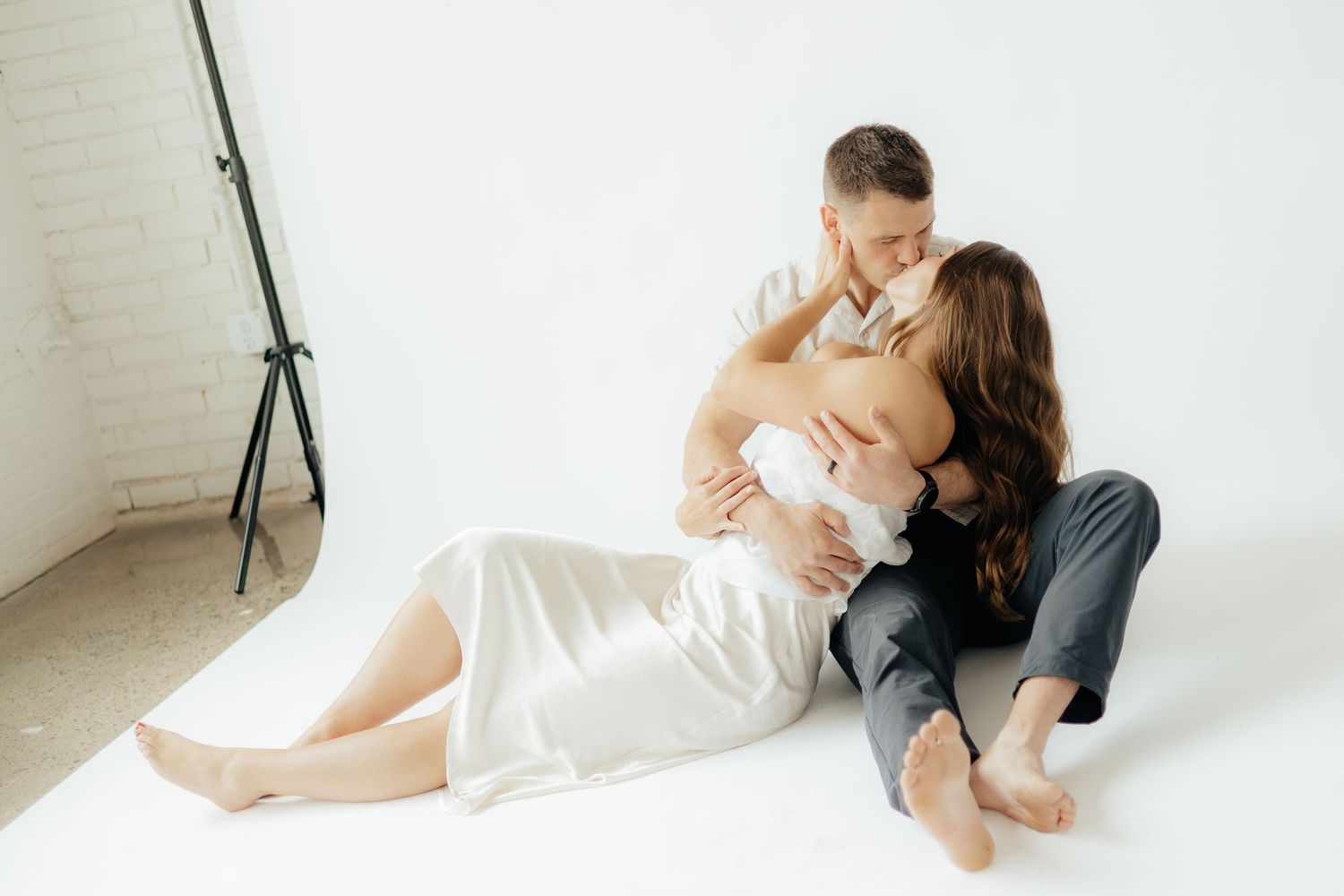 Couple embracing in soft natural light at Abide Studio in Minneapolis, MN, with minimalist white walls and warm, cozy tones