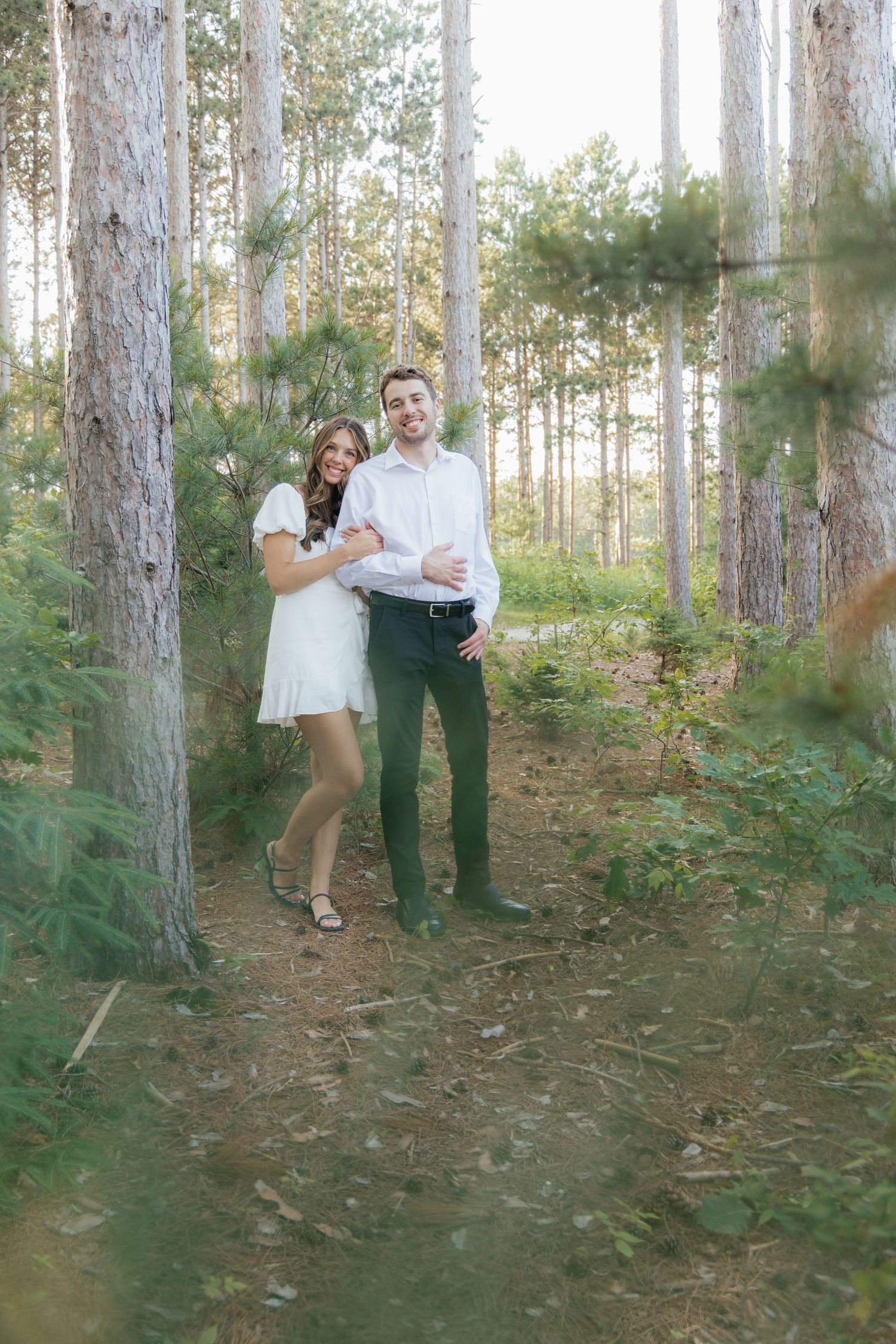 Golden-hour portrait of a couple embracing among tall trees at Pinewood in Cambridge, showcasing woodsy elegance.