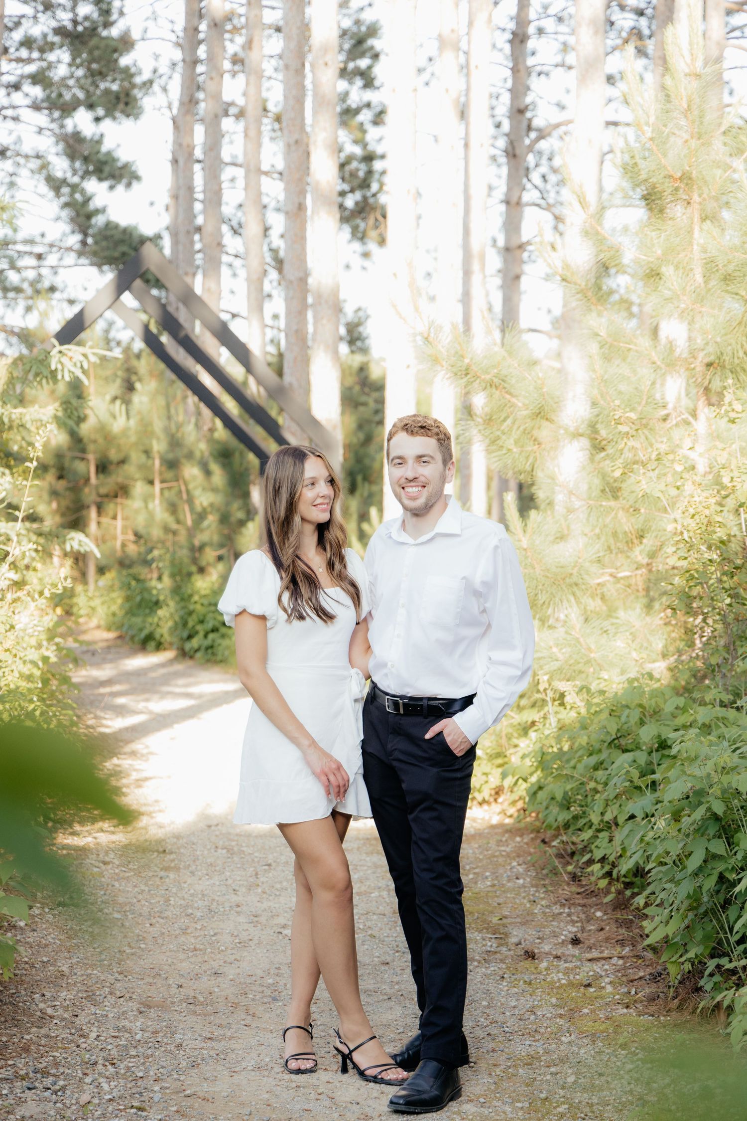 Golden-hour portrait of a couple embracing among tall trees at Pinewood in Cambridge, showcasing woodsy elegance.