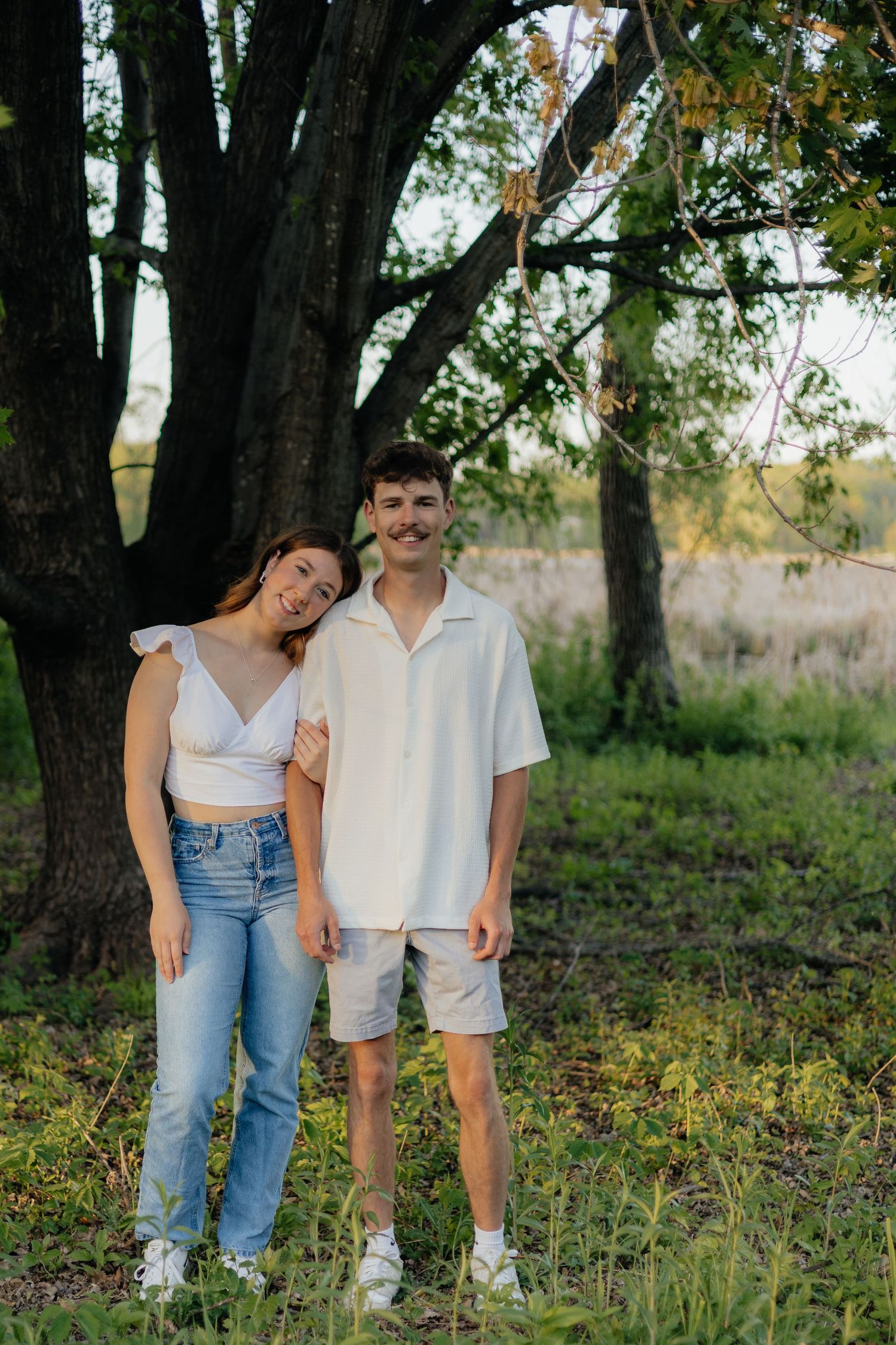 Couple smiling together along the lakeshore at Fish Lake Regional Park in Maple Grove, MN, with bright green trees and clear blue water