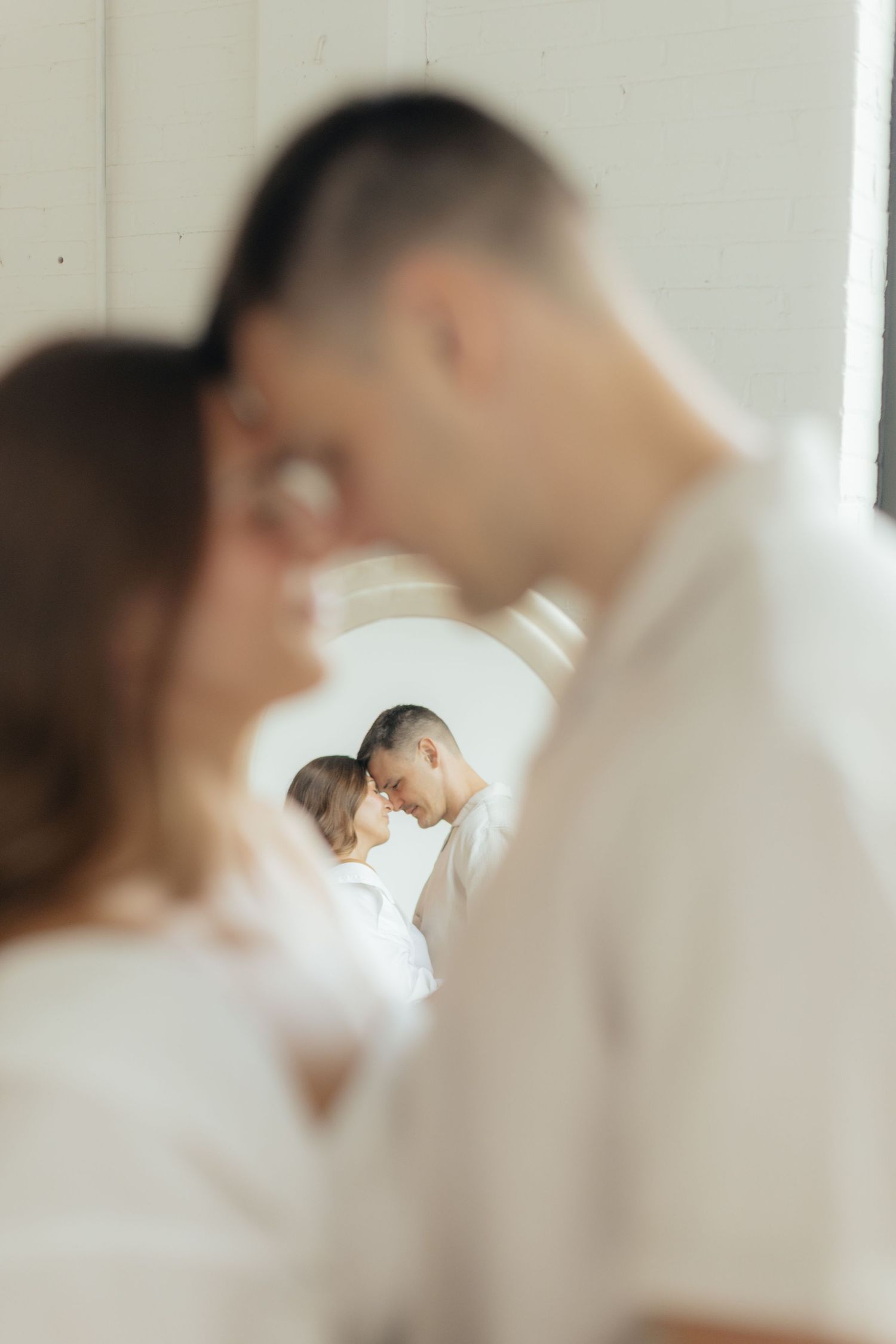 Couple embracing in soft natural light at Abide Studio in Minneapolis, MN, with minimalist white walls and warm, cozy tones