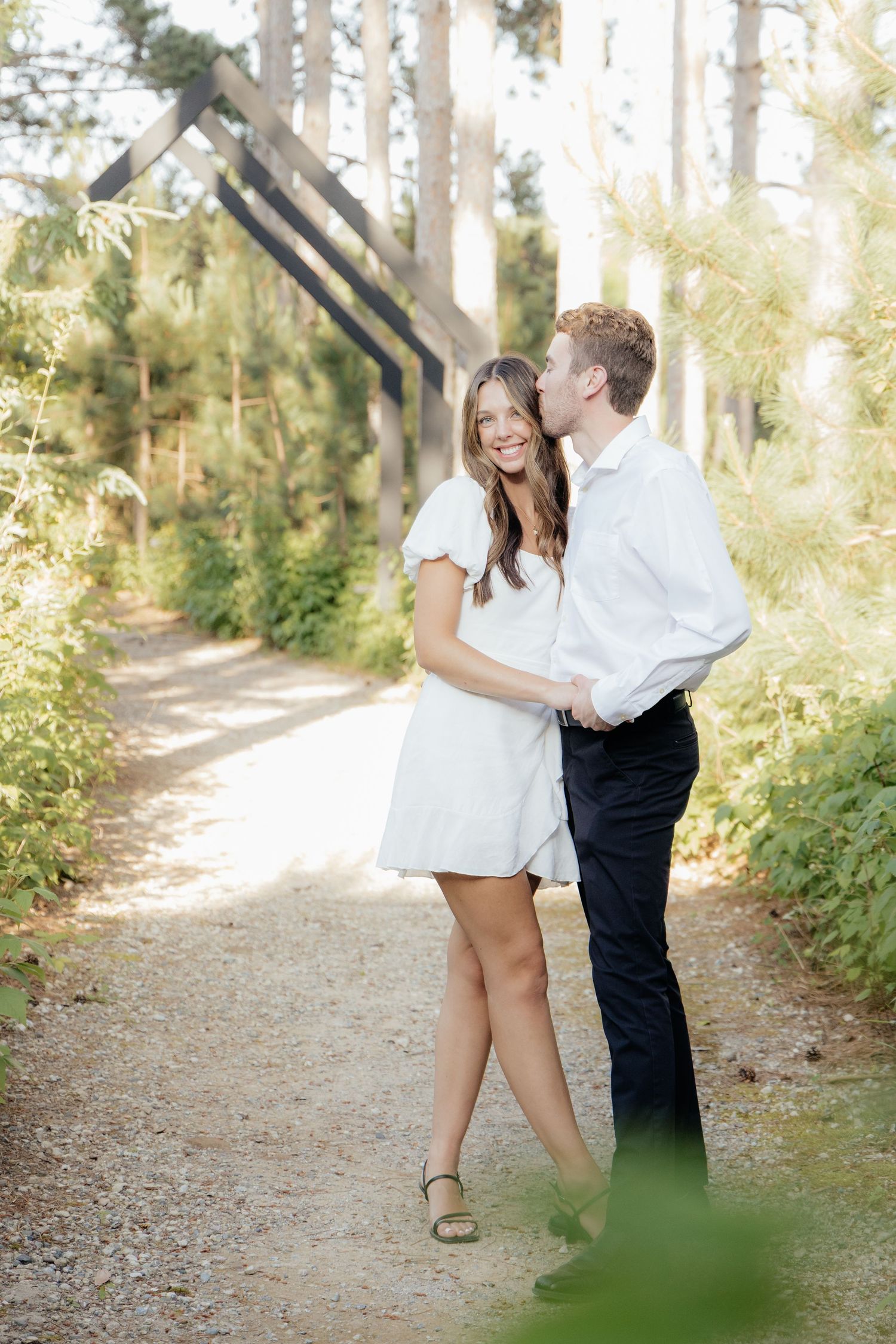 Golden-hour portrait of a couple embracing among tall trees at Pinewood in Cambridge, showcasing woodsy elegance.