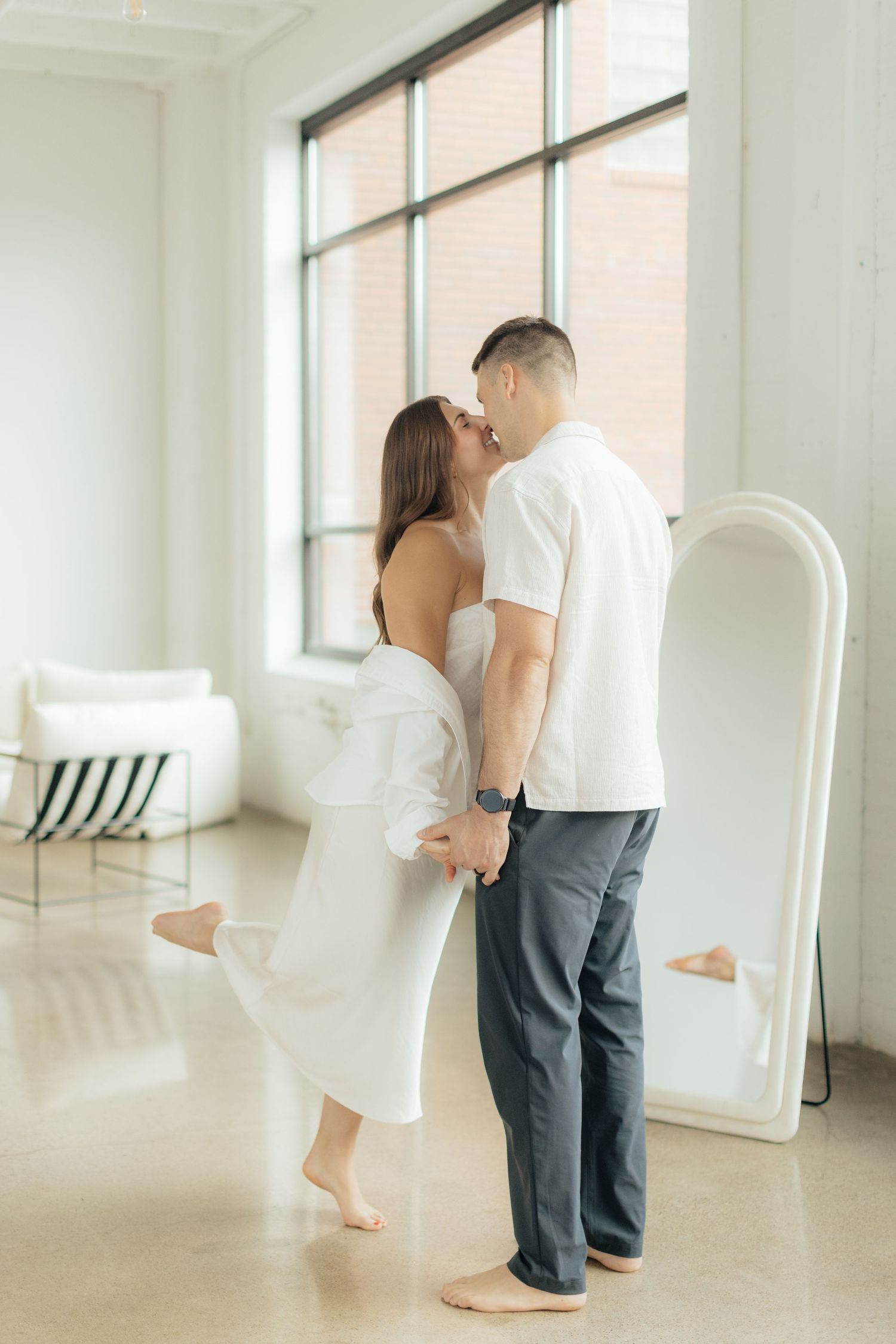 Couple embracing in soft natural light at Abide Studio in Minneapolis, MN, with minimalist white walls and warm, cozy tones