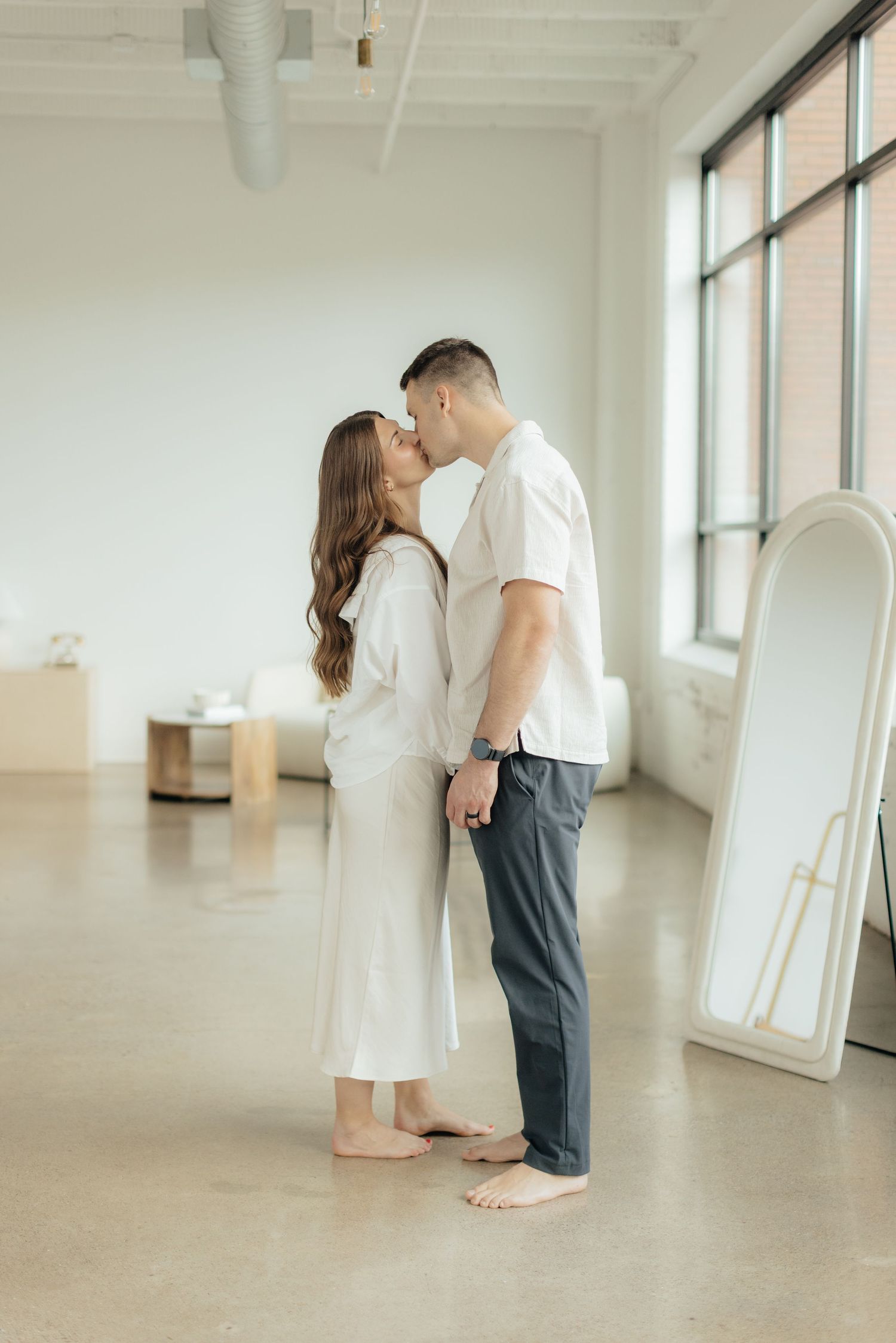 Couple embracing in soft natural light at Abide Studio in Minneapolis, MN, with minimalist white walls and warm, cozy tones